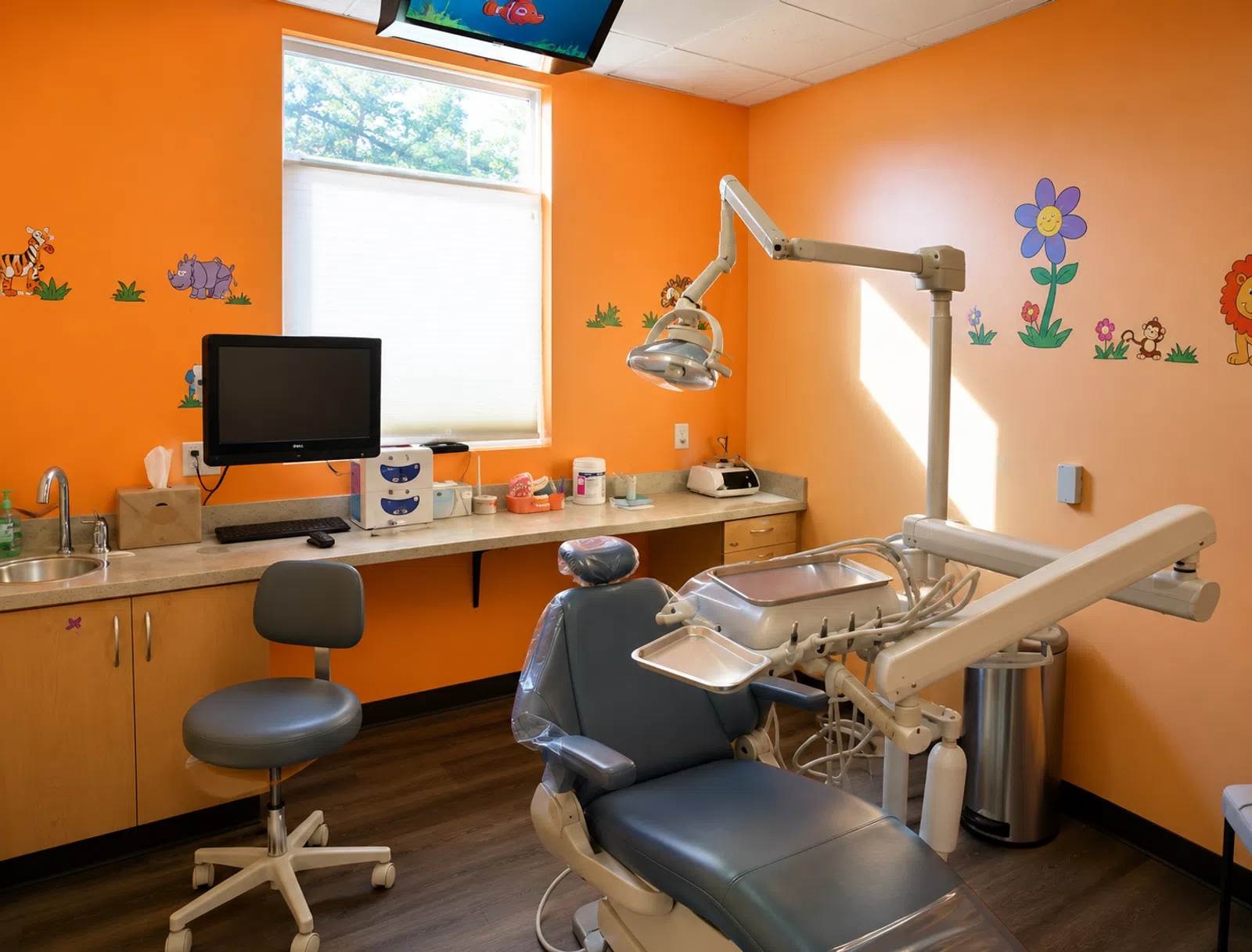 Bright orange pediatric dental office with dental chair, monitor, and colorful animal wall decals.