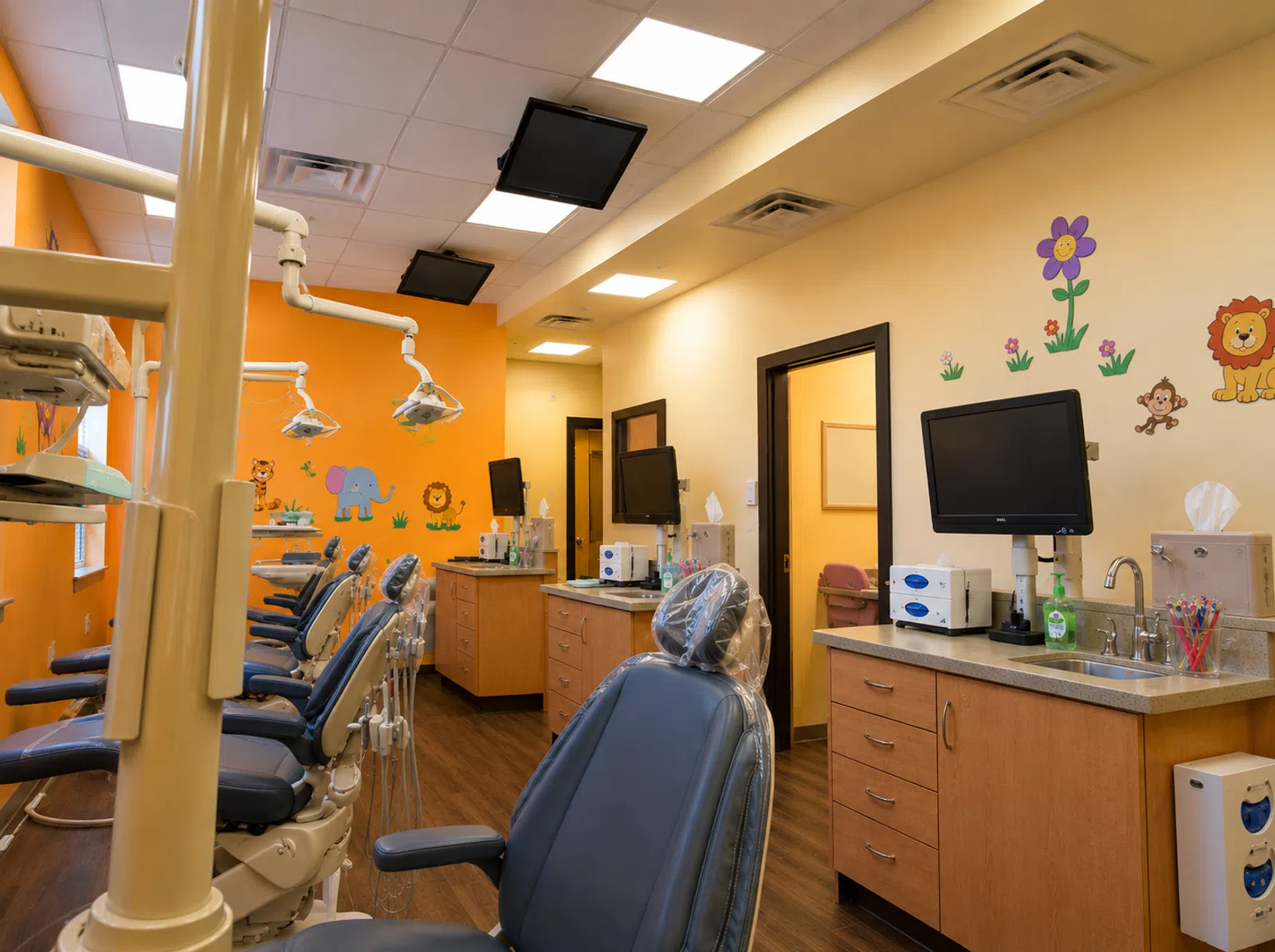Bright pediatric dental office with colorful animal wall decals, multiple dental chairs, and mounted TVs.