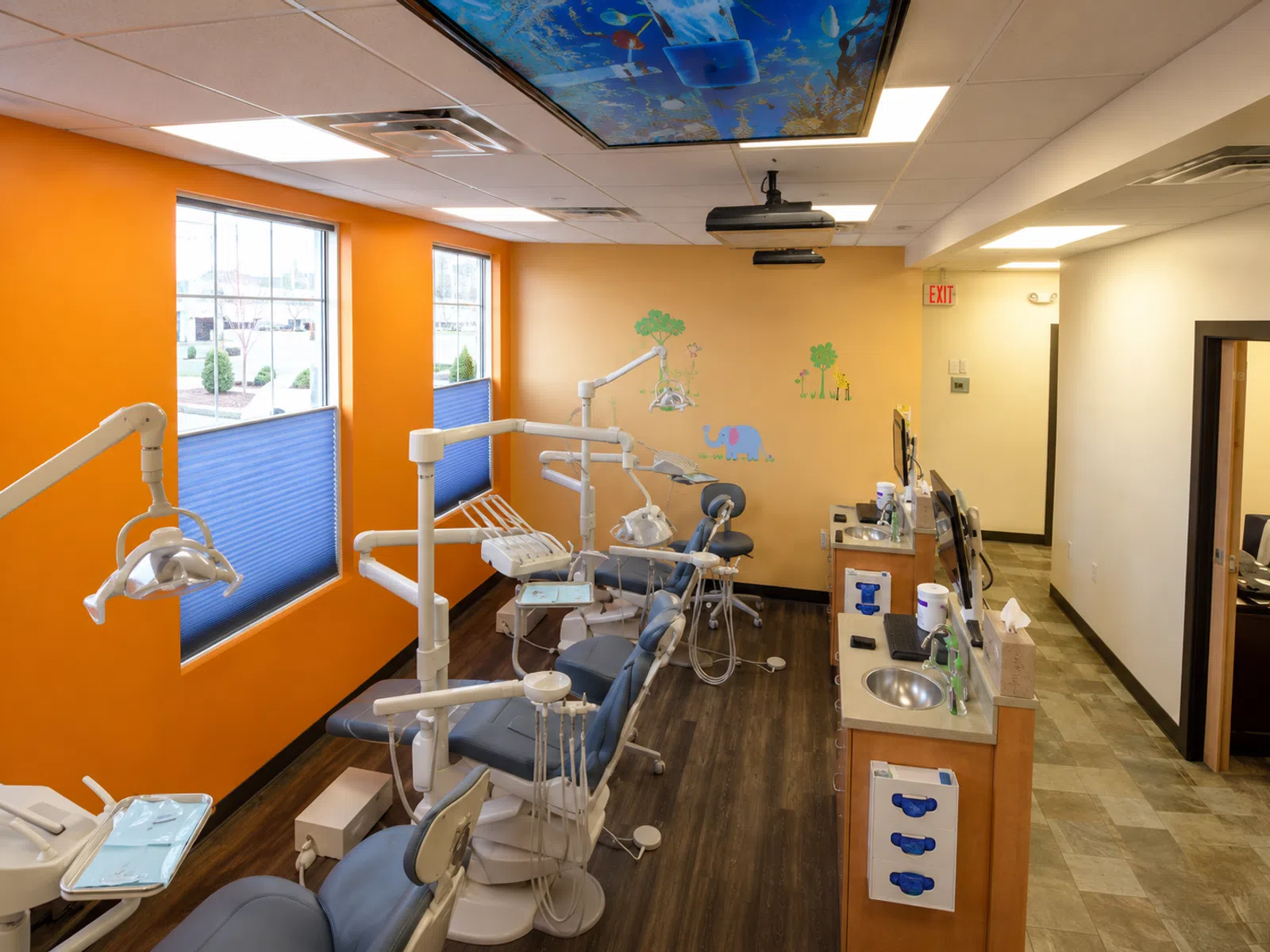 Bright pediatric dental clinic with multiple dental chairs, colorful walls, and a ceiling ocean mural.