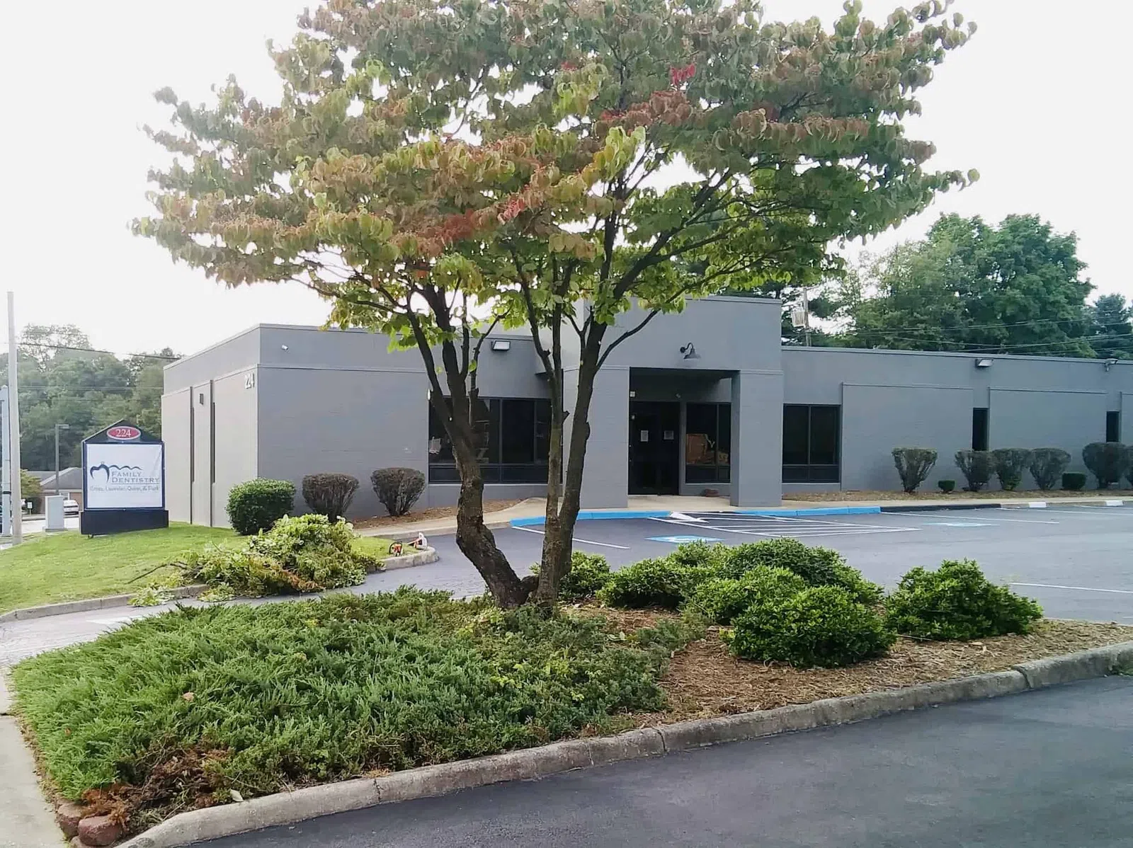 Gray office building with landscaped greenery and parking lot under a partly cloudy sky.