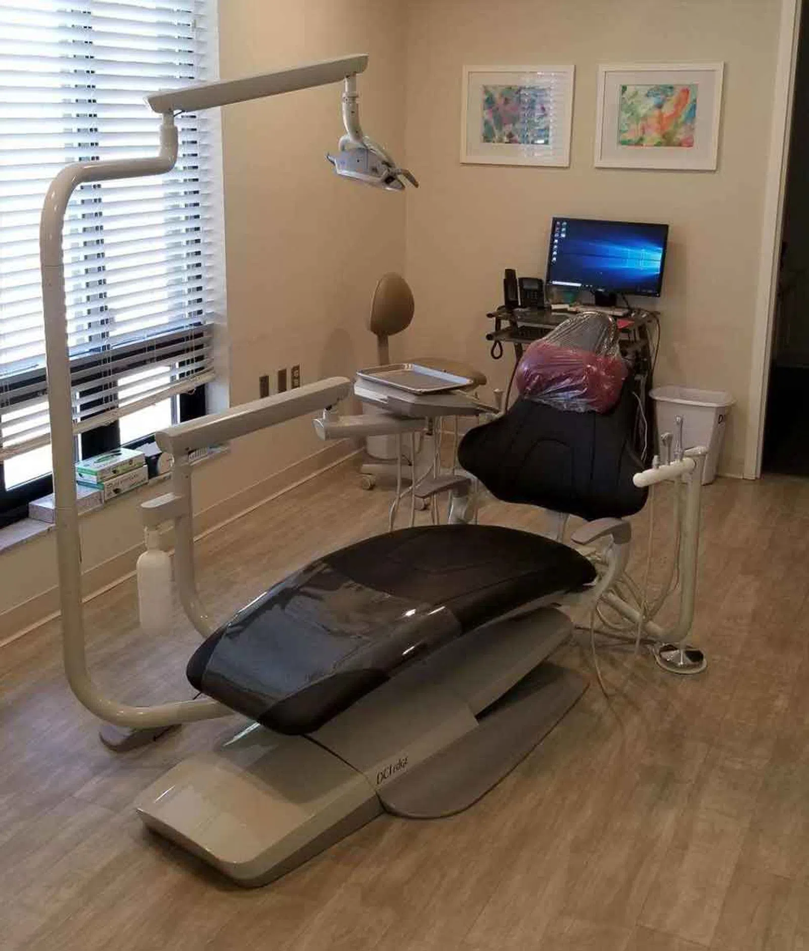 Modern dental clinic room with a reclining patient chair, overhead light, computer, and medical equipment.
