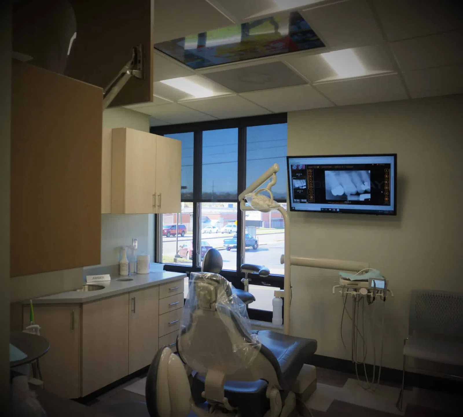 Modern dental office with exam chair, dental equipment, cabinets, and X-ray displayed on wall-mounted screen.