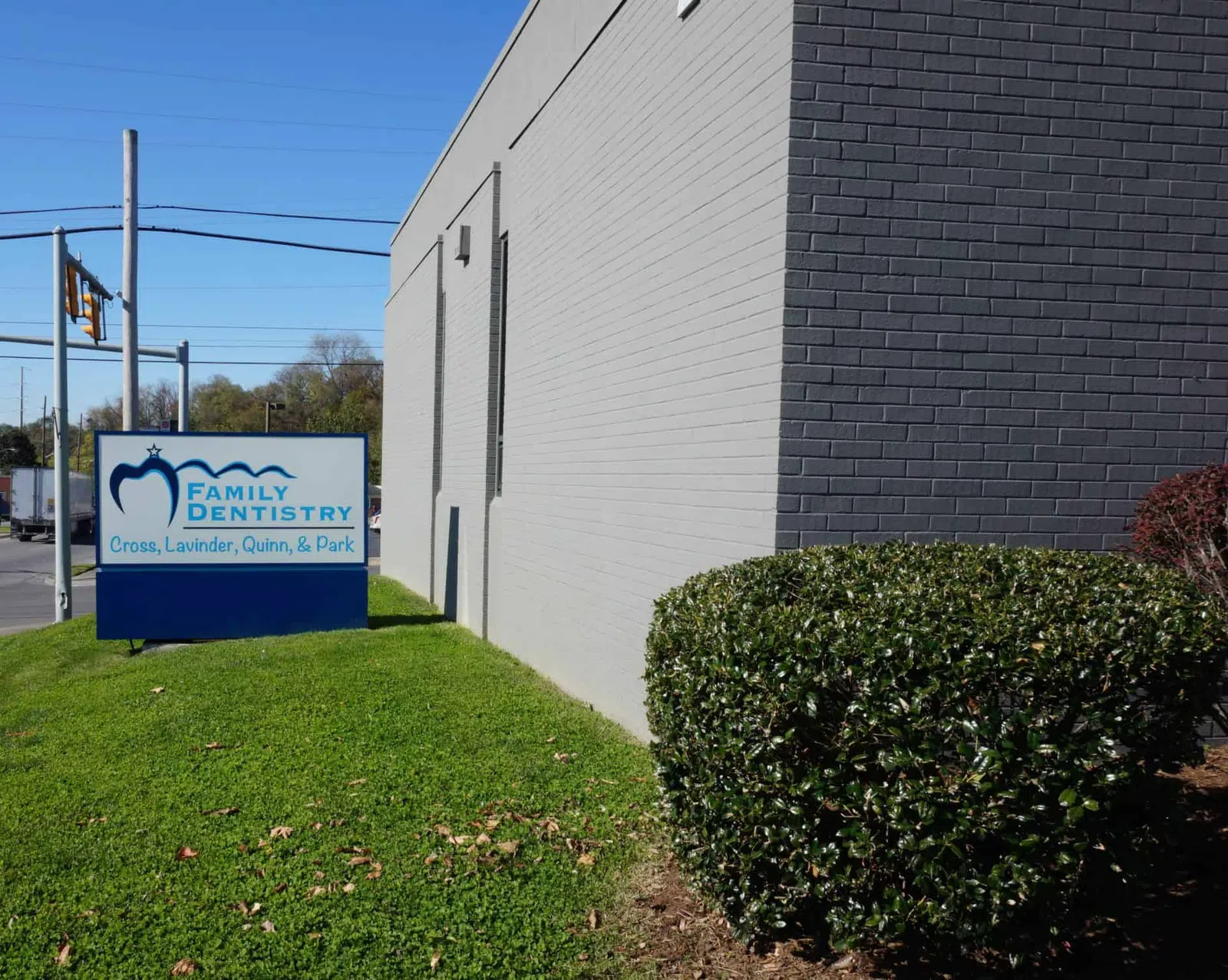 Family Dentistry sign near gray brick building with green lawn and bush under clear blue sky.
