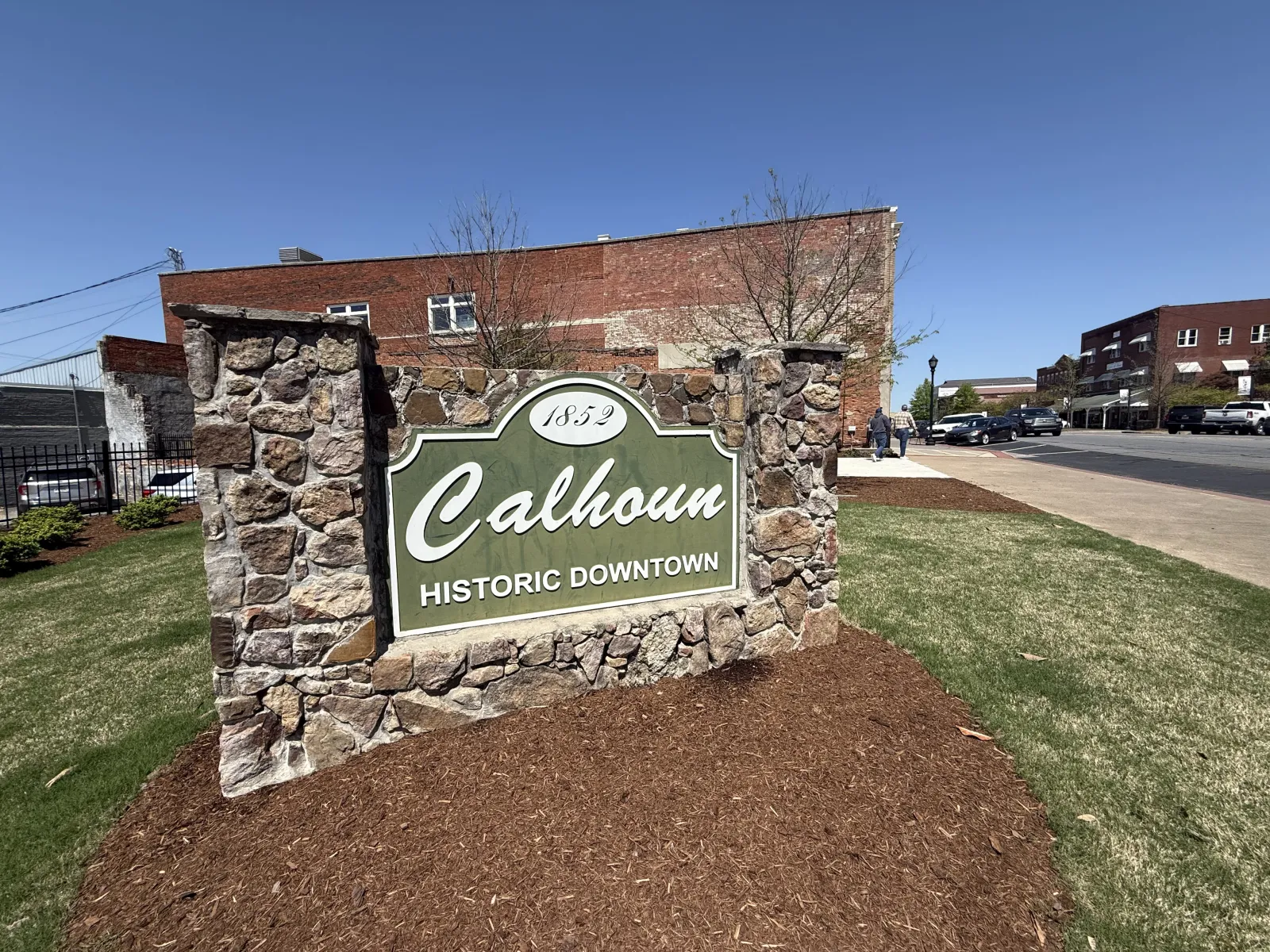 Stone sign for Calhoun Historic Downtown established 1852 with red brick buildings and cars on clear day