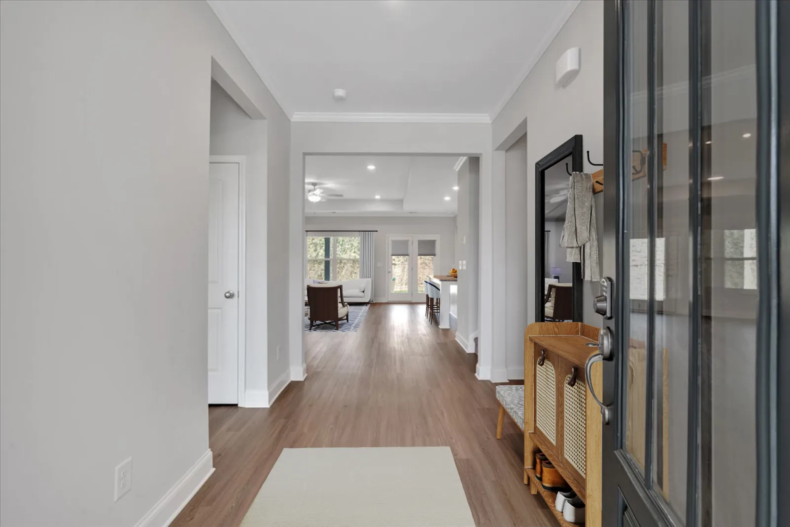 Modern home entryway with wooden flooring, white walls, and open view into living and kitchen areas with natural light.
