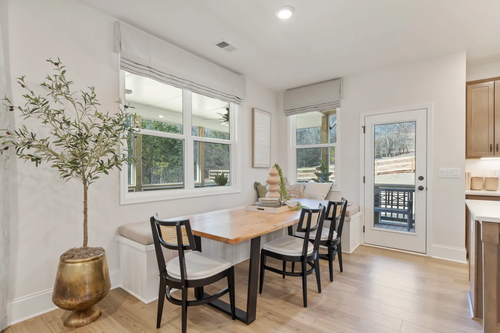 Bright dining nook with wooden table, black chairs, window seating, and potted plant in modern home