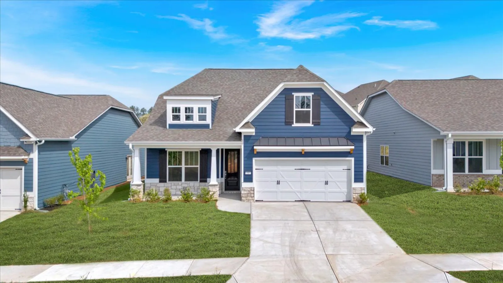 Blue two-story suburban house with white trim, attached garage, manicured lawn, and clear blue sky.