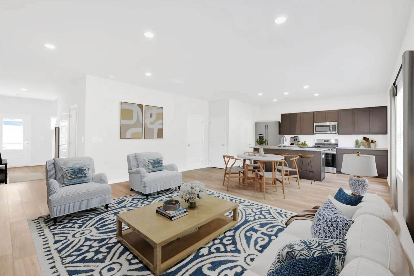 Bright open living room with blue patterned rug, white sofa, armchairs, wooden coffee table, and modern kitchen in background