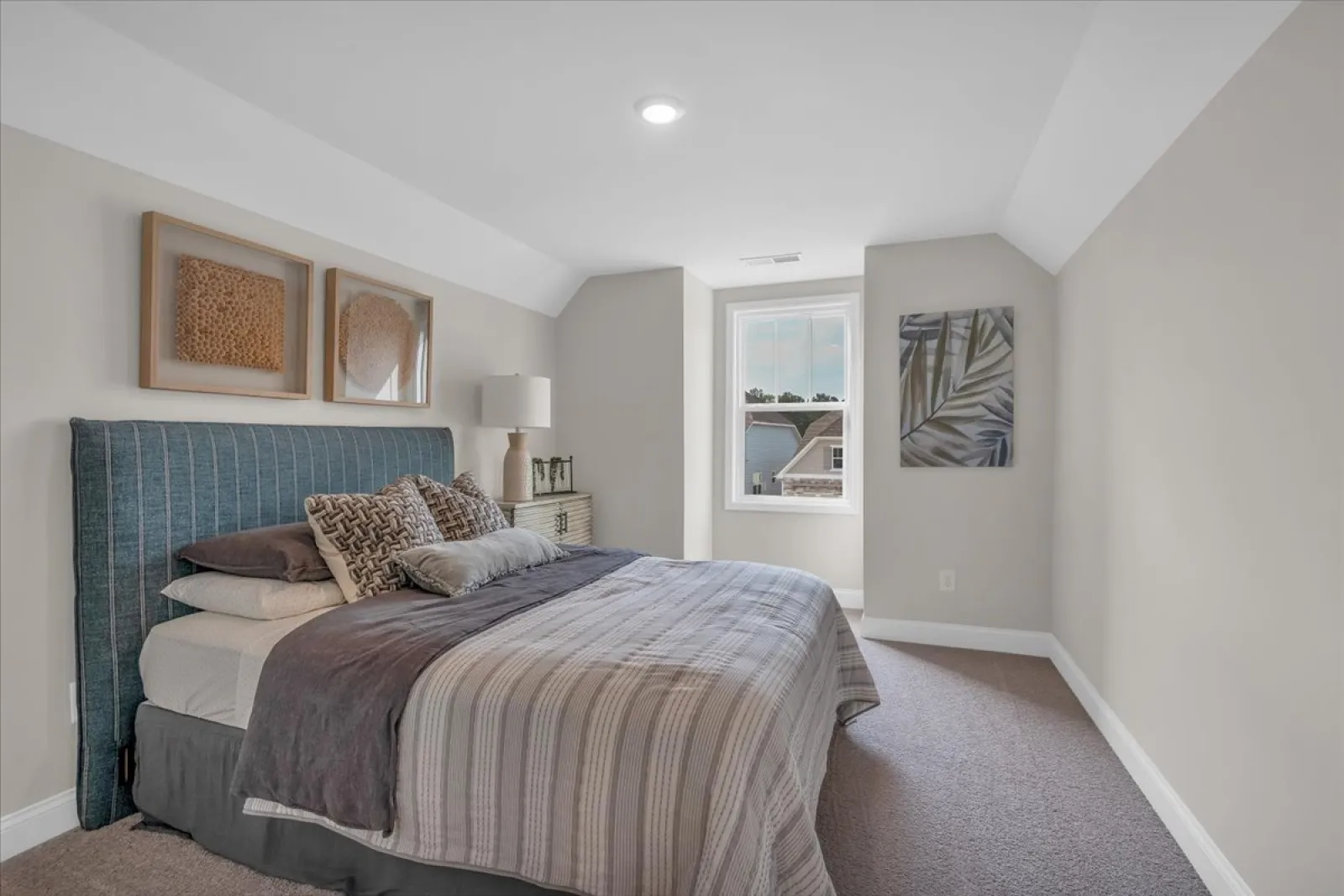 Bright modern bedroom with large bed, blue upholstered headboard, textured pillows, and natural light from a window.