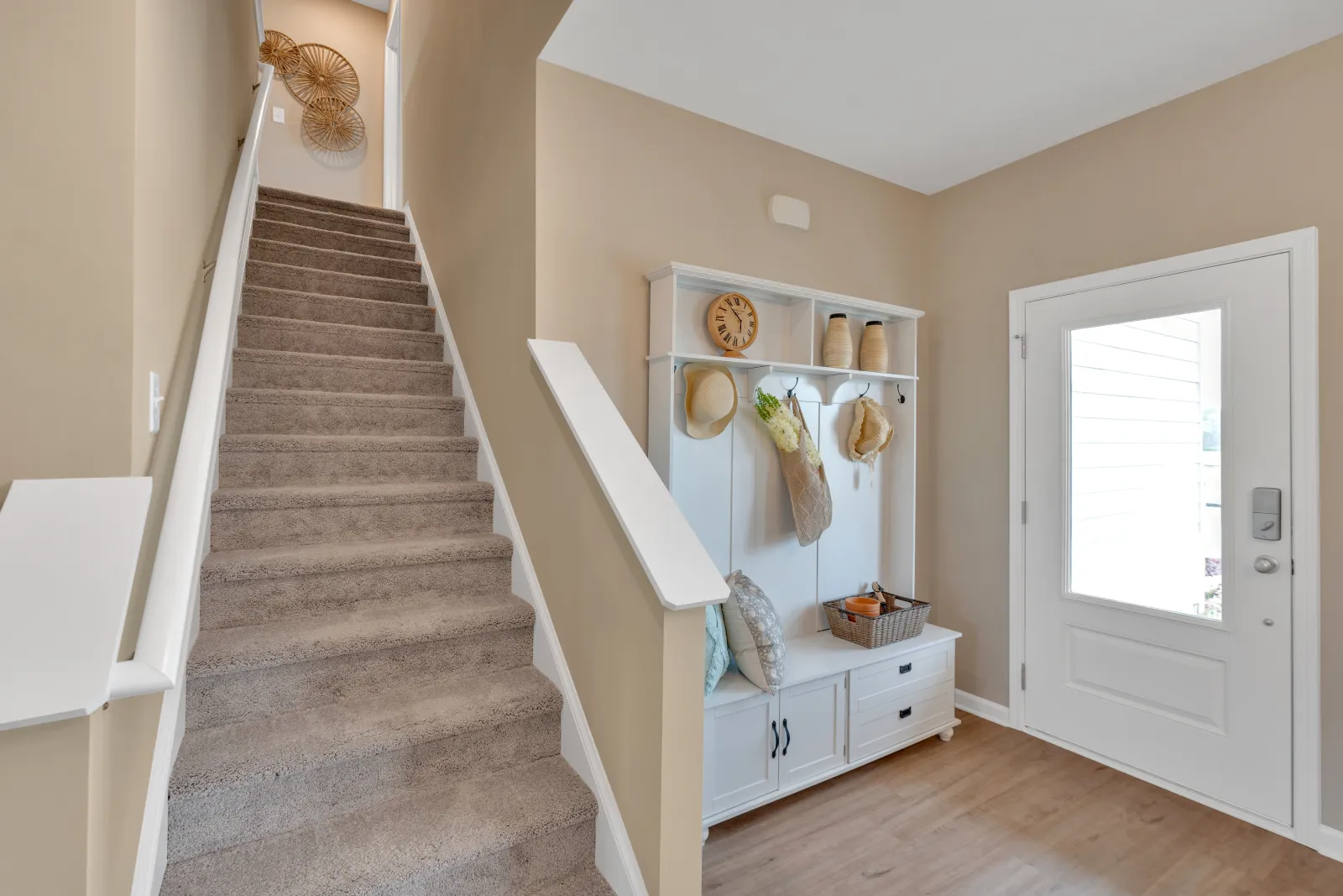 Welcoming entryway with stairs, coat rack, and decor in a light beige and white color palette.