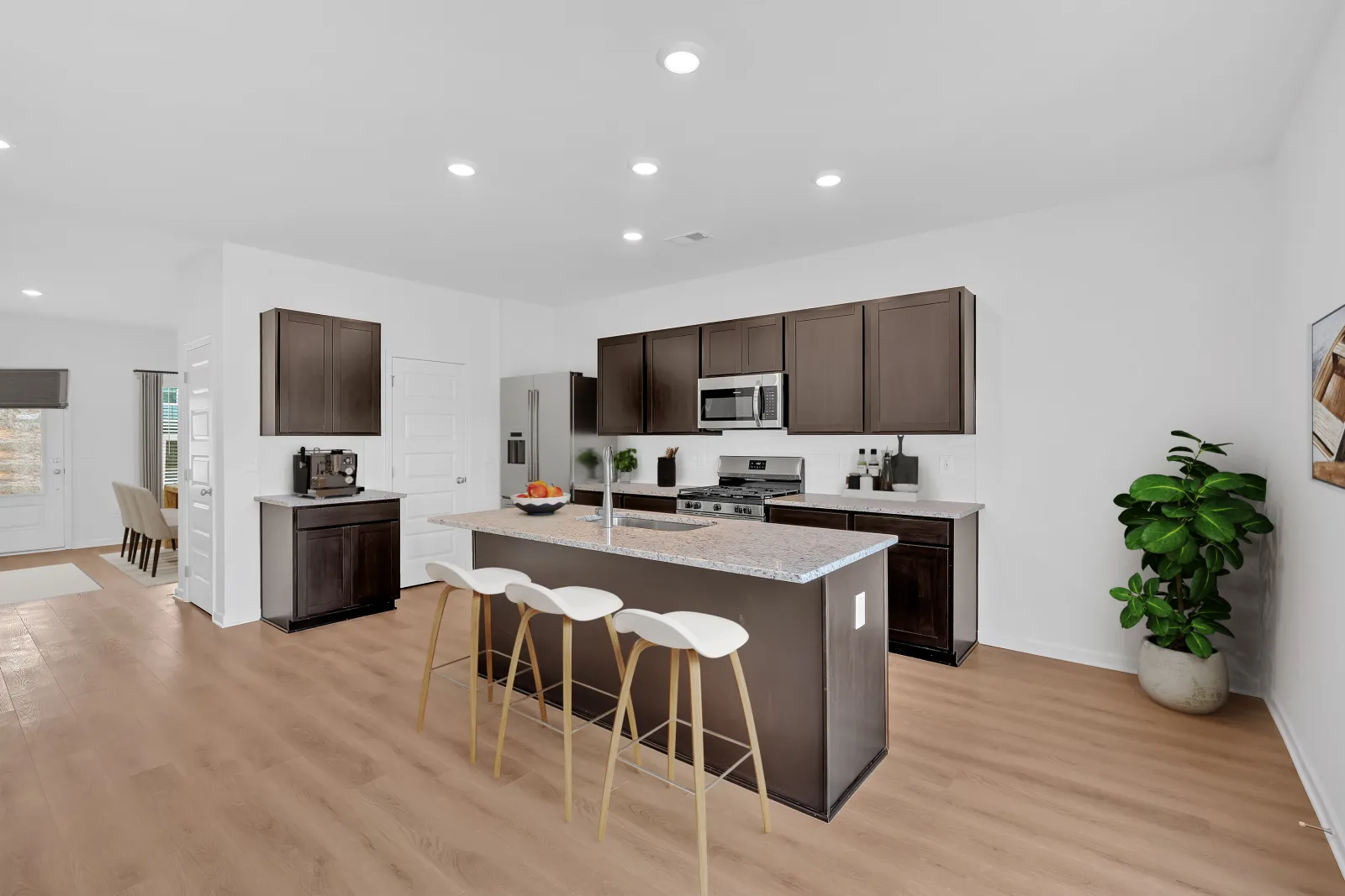 Modern kitchen with dark wood cabinets, granite island, white bar stools, stainless appliances, and light hardwood floors