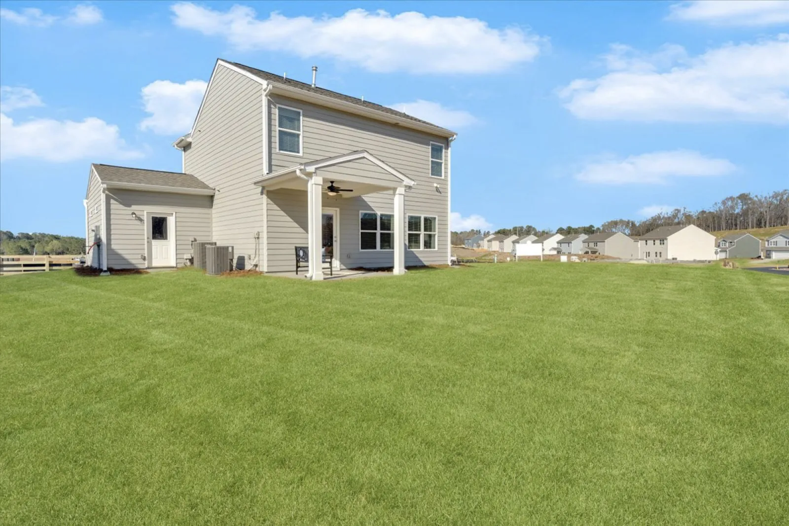 Charming two-story house with a spacious green lawn under a blue sky.