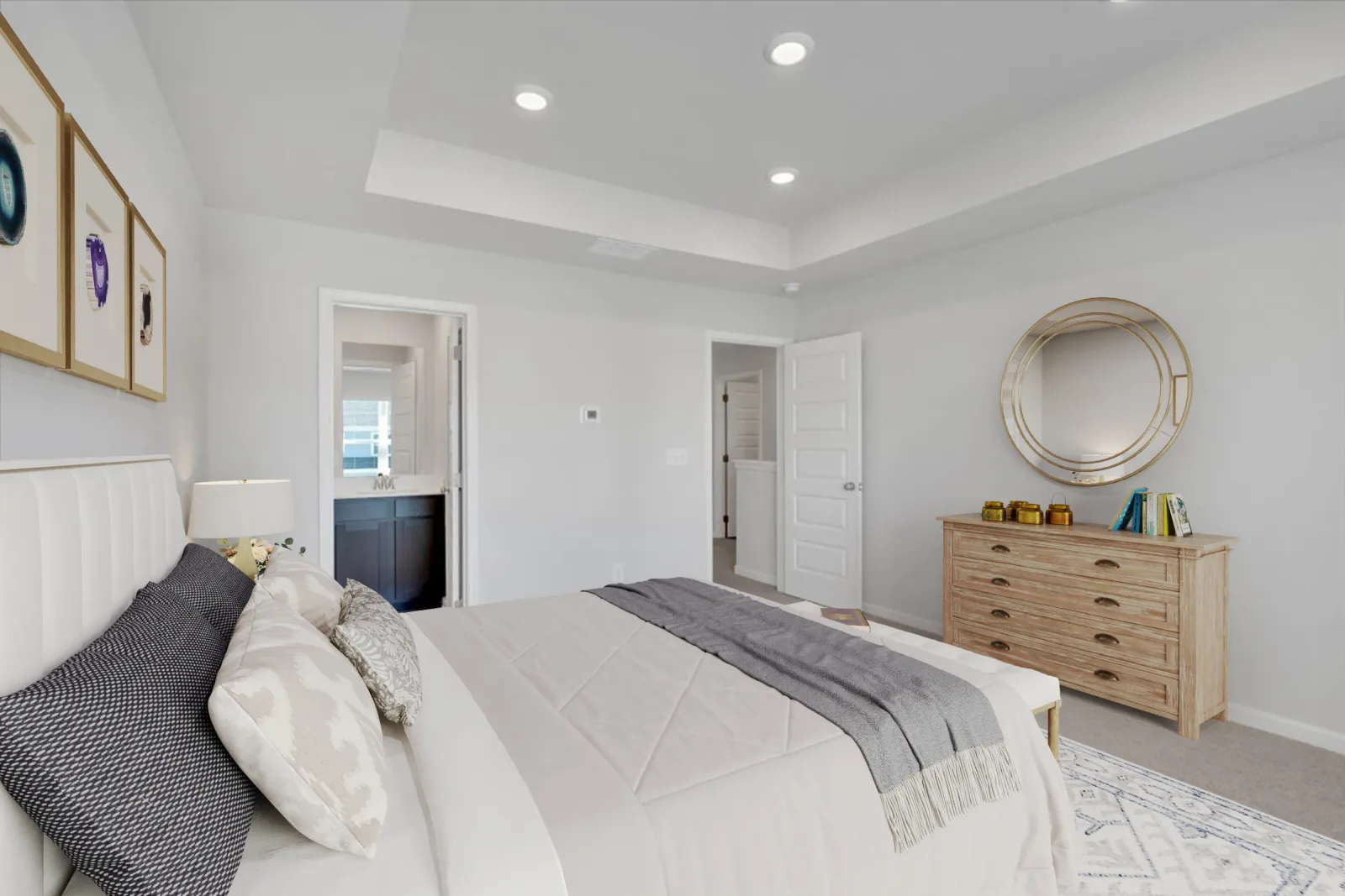 Bright modern bedroom featuring a large bed, soft gray bedding, wooden dresser, and round mirror on white walls.