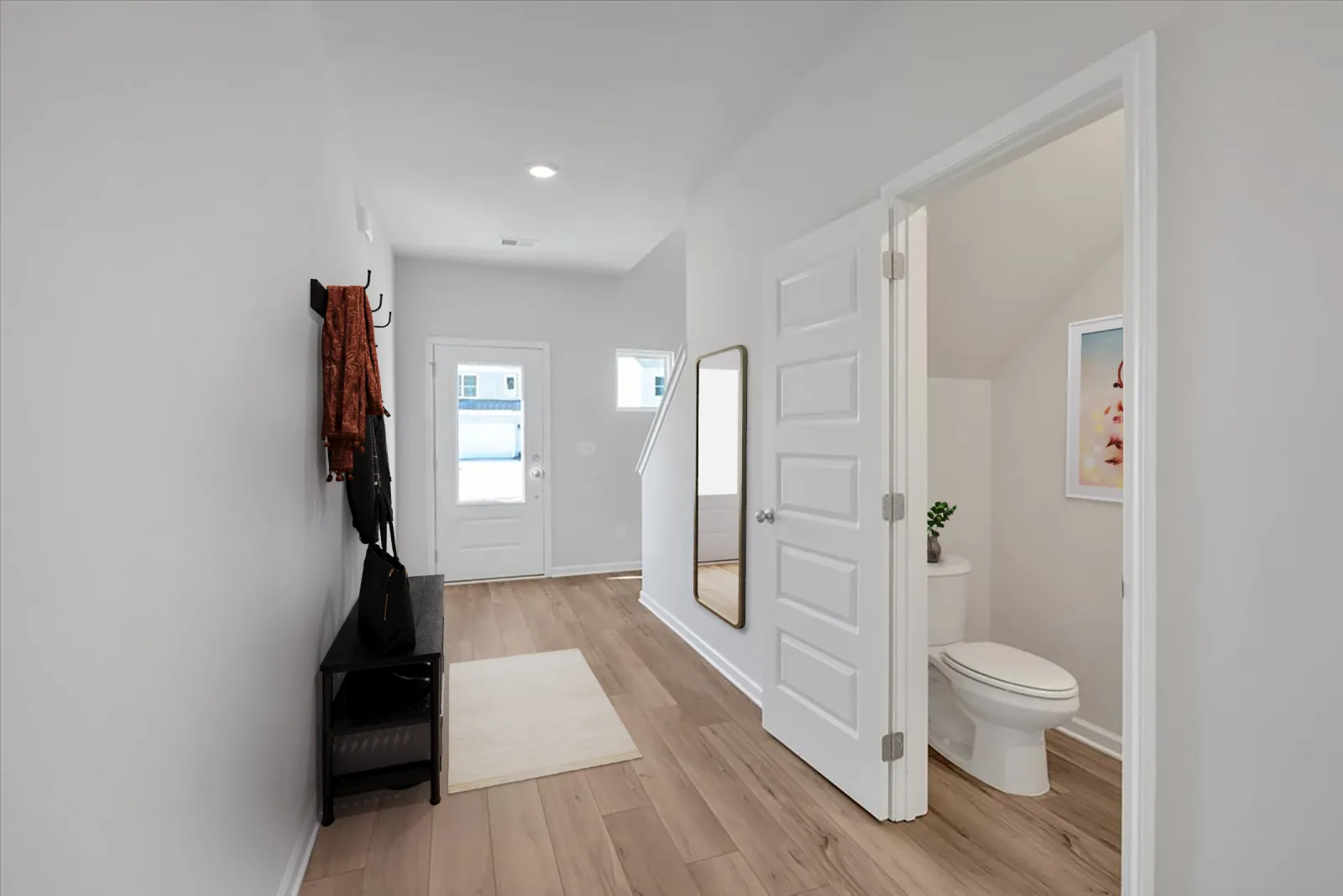 Bright hallway with wooden floor, a mirror on the wall, a small bench, and an open door to a bathroom.