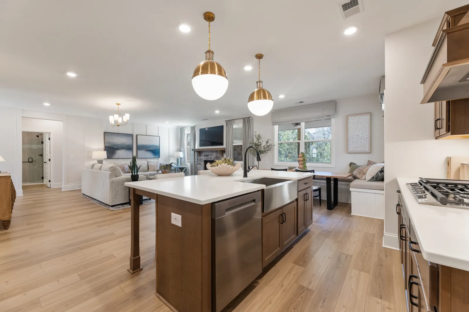 Modern open-concept kitchen with wood floors, island with lighting, and a living area with a fireplace and large windows.