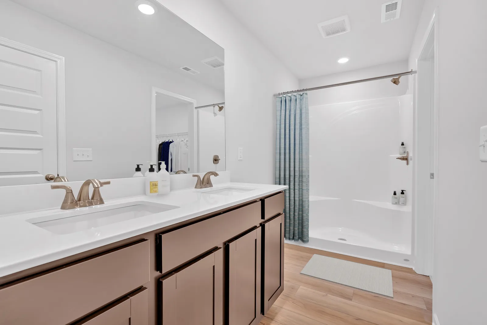 Bright modern bathroom with double sinks, a spacious shower, and light wood flooring.