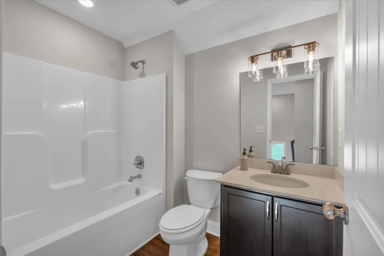 Modern bathroom with white bathtub, toilet, dark wood vanity, and mirror under bright light fixtures