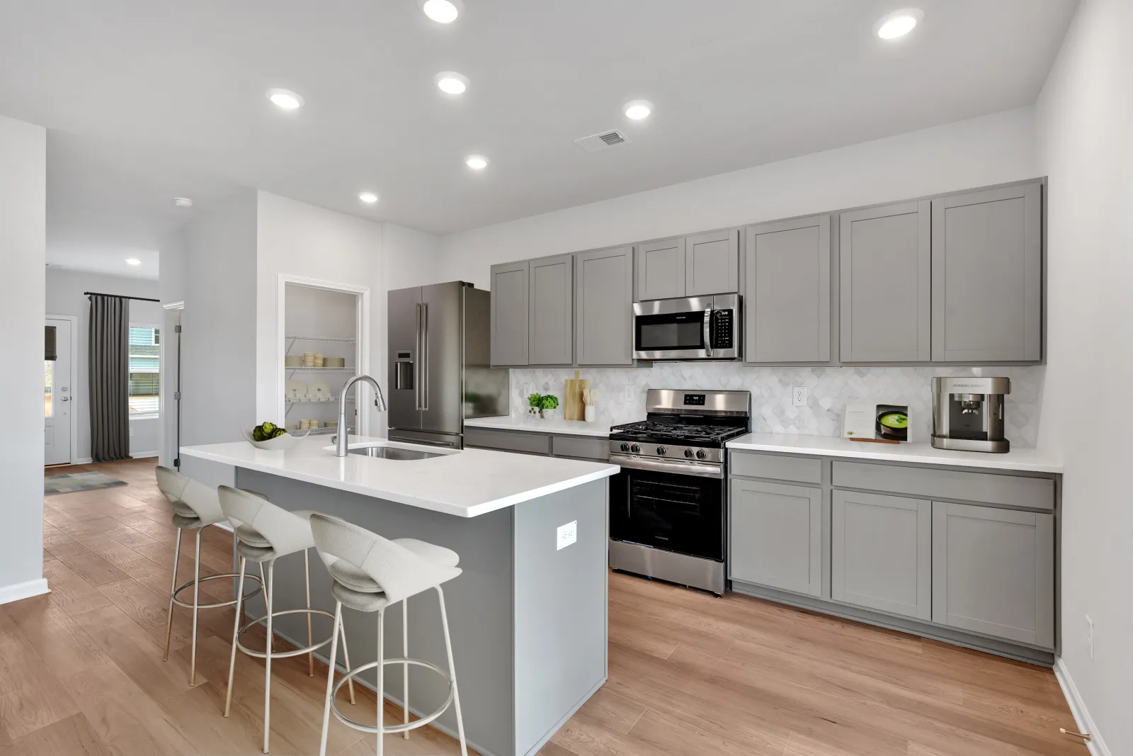 Modern kitchen with gray cabinets, white countertops, stainless steel appliances, and a kitchen island with bar stools.