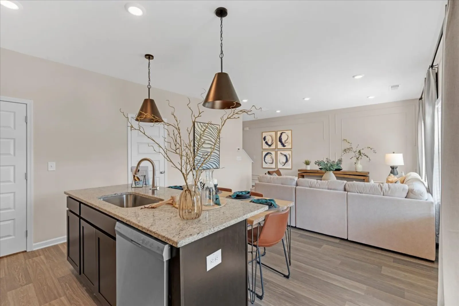 Modern kitchen with pendant lights and a cozy living area in the background, featuring stylish decor.
