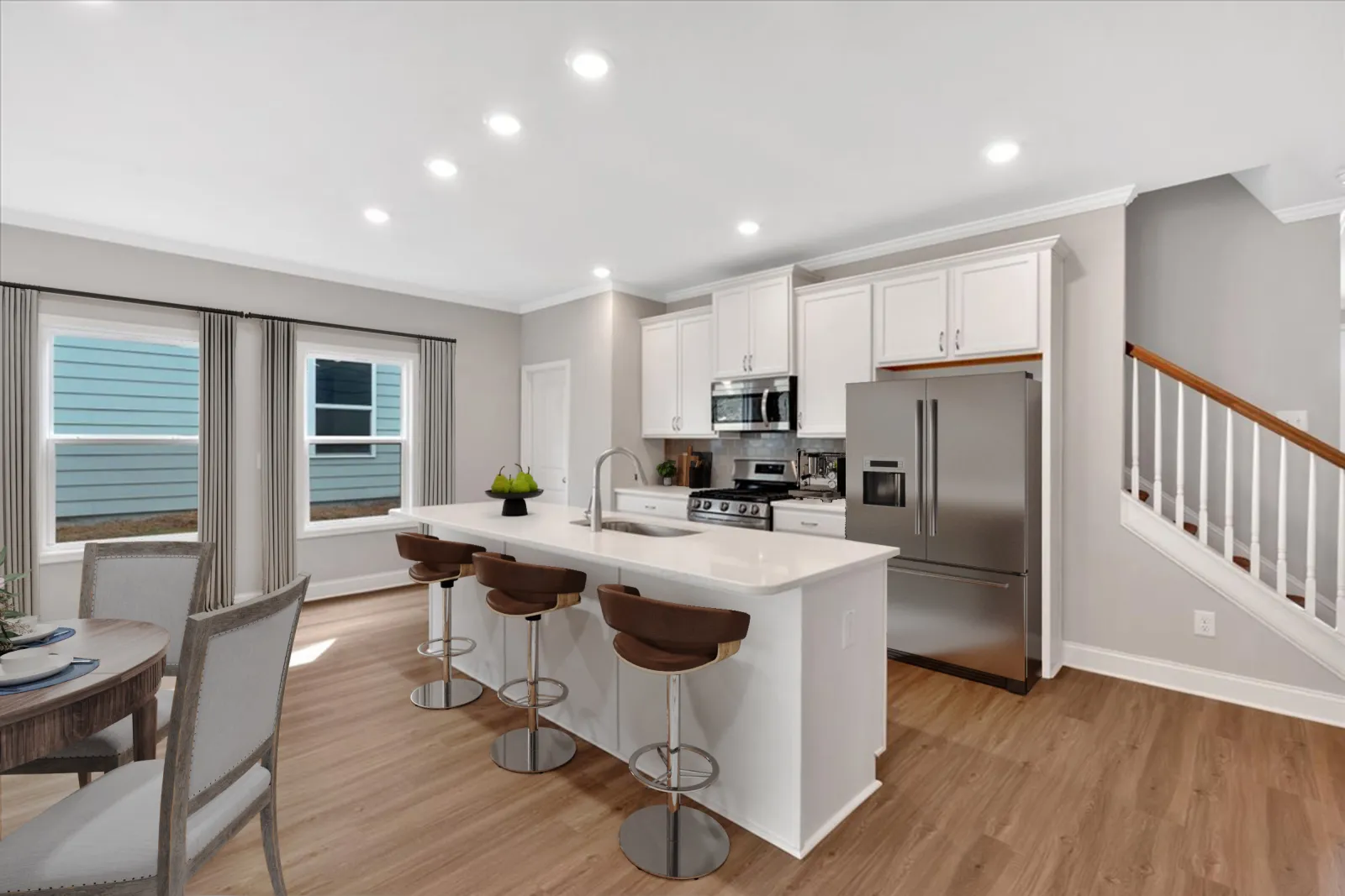 Modern white kitchen with island, stainless steel appliances, wooden bar stools, and dining area with natural light.