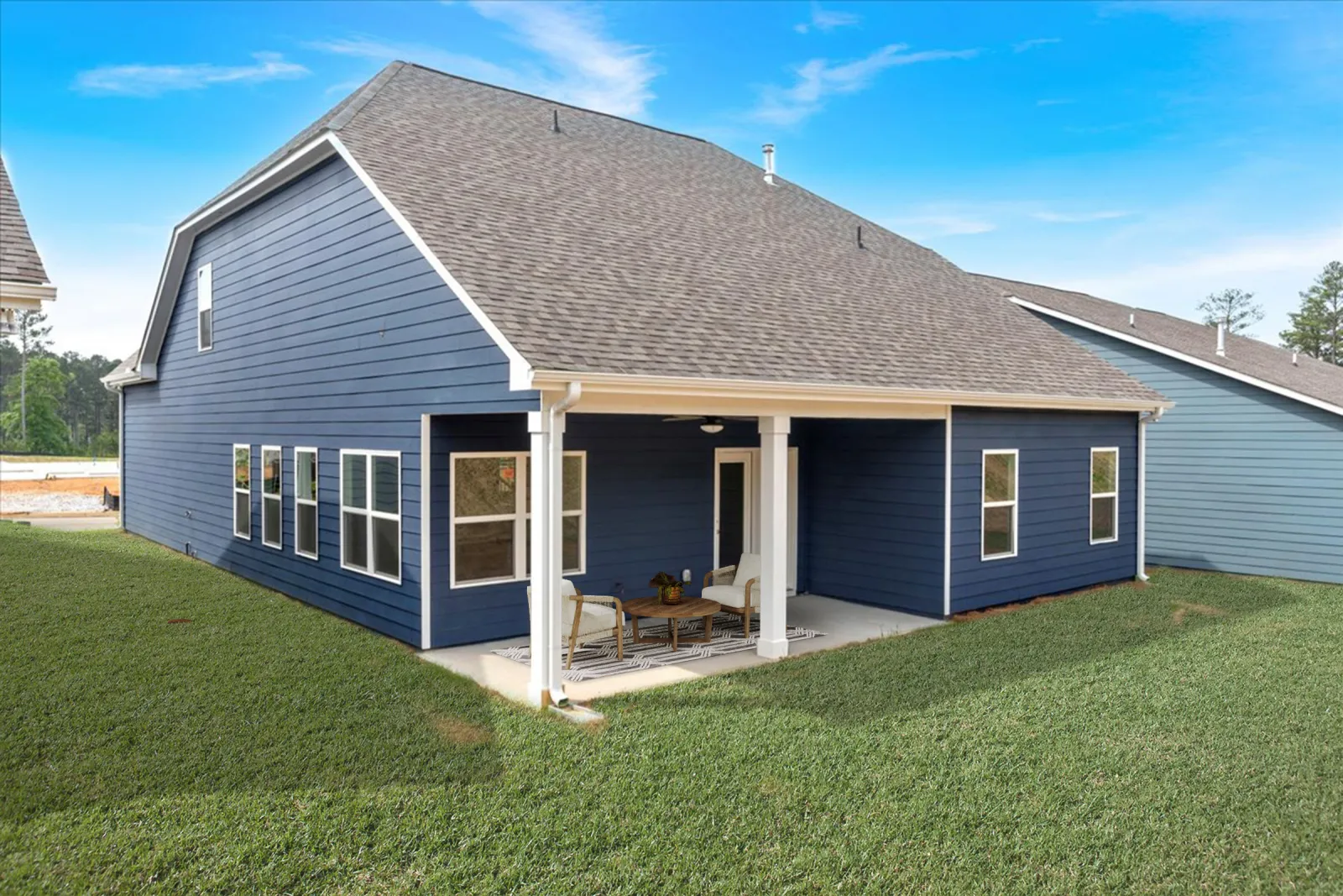 Modern blue house with white trim features a covered patio with outdoor seating overlooking green lawn under blue sky.