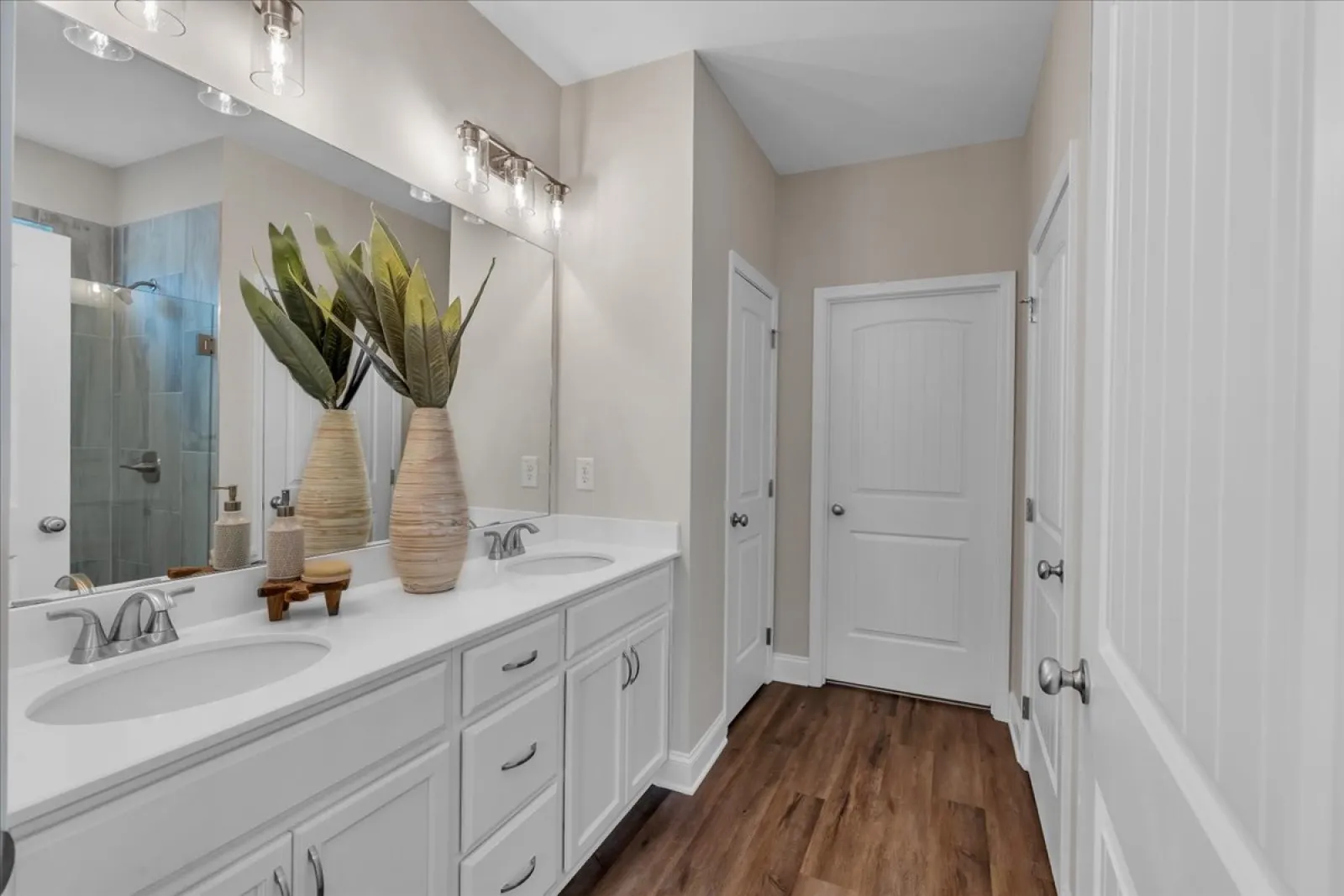 Bright modern bathroom with double sinks, large mirror, wooden floor, and decorative plants on countertop