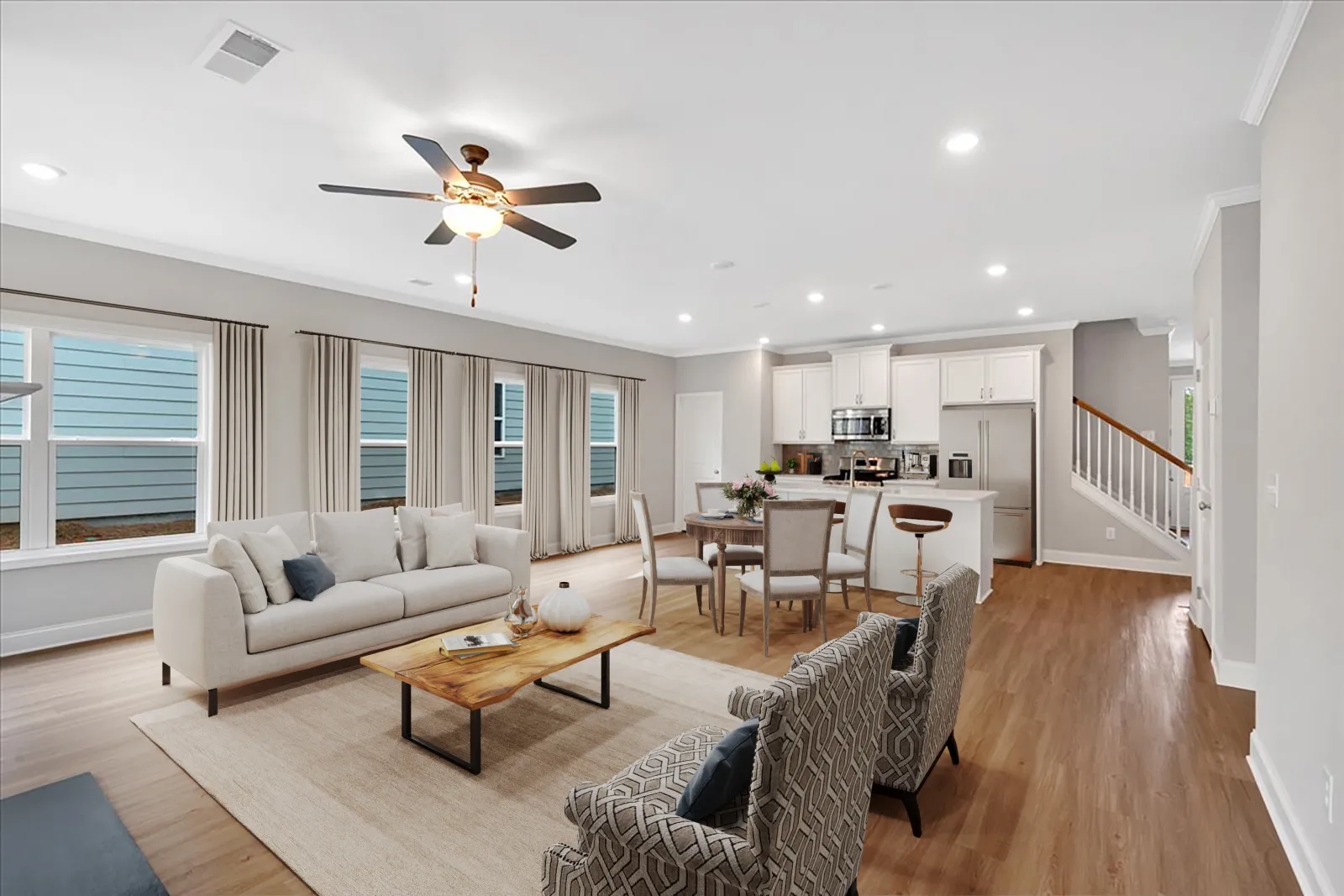 Bright open-concept living room with beige sofa, patterned armchairs, wood coffee table, dining set, and modern kitchen.