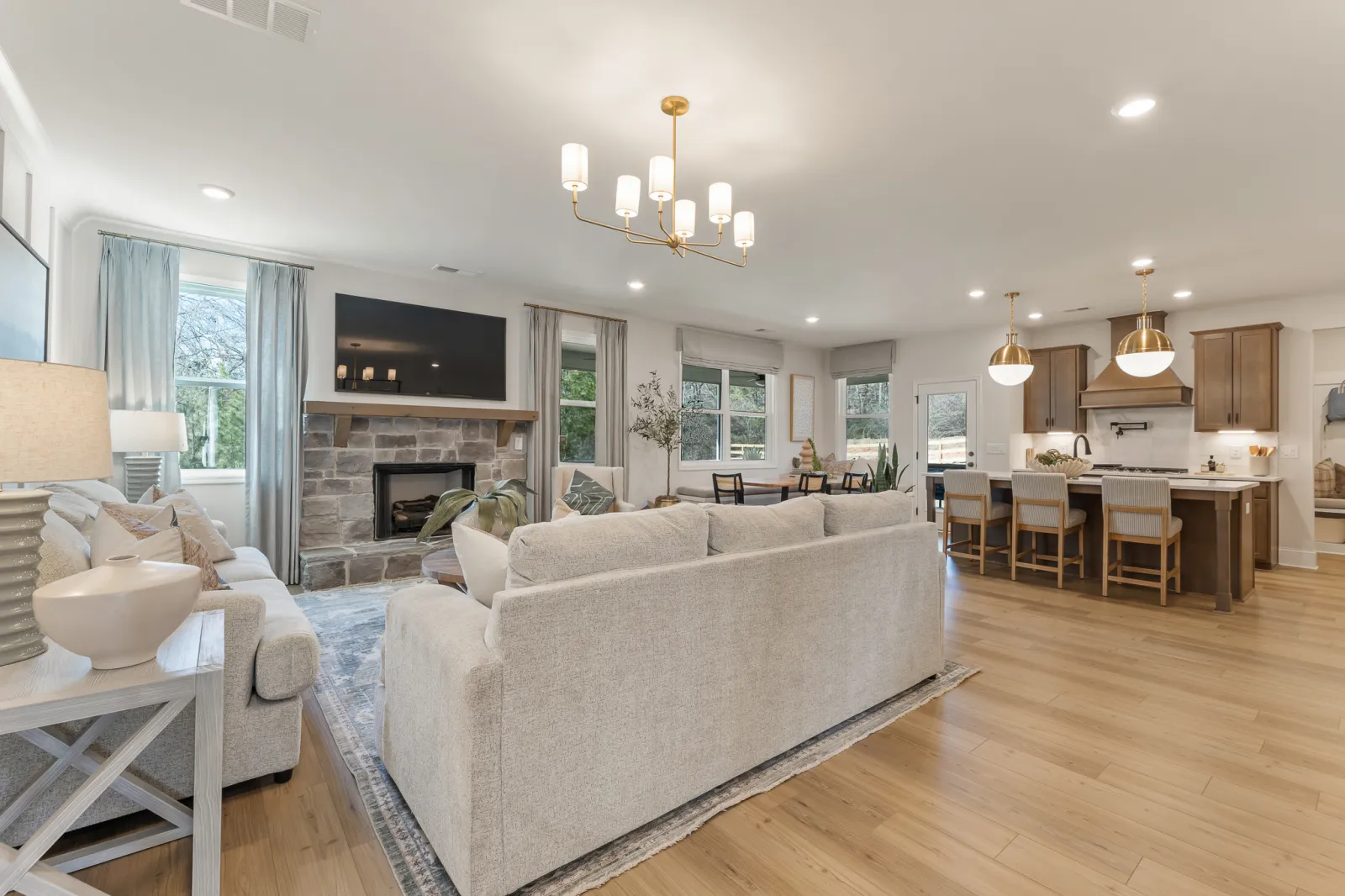 Spacious open-concept living room and kitchen with neutral furniture, hardwood floors, and modern lighting fixtures