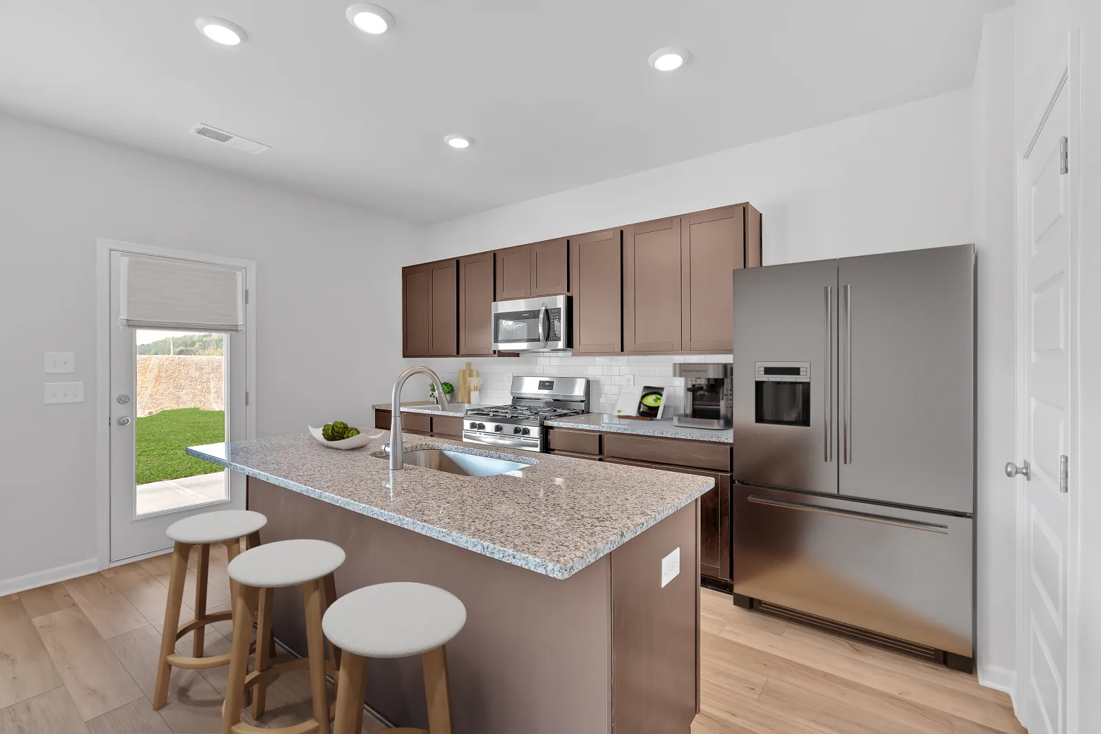 Modern kitchen with granite island, stainless steel appliances, and wooden accents, featuring natural light from windows.
