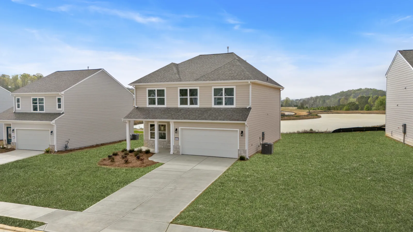 Modern two-story house with beige siding, a two-car garage, and spacious front lawn under a blue sky.
