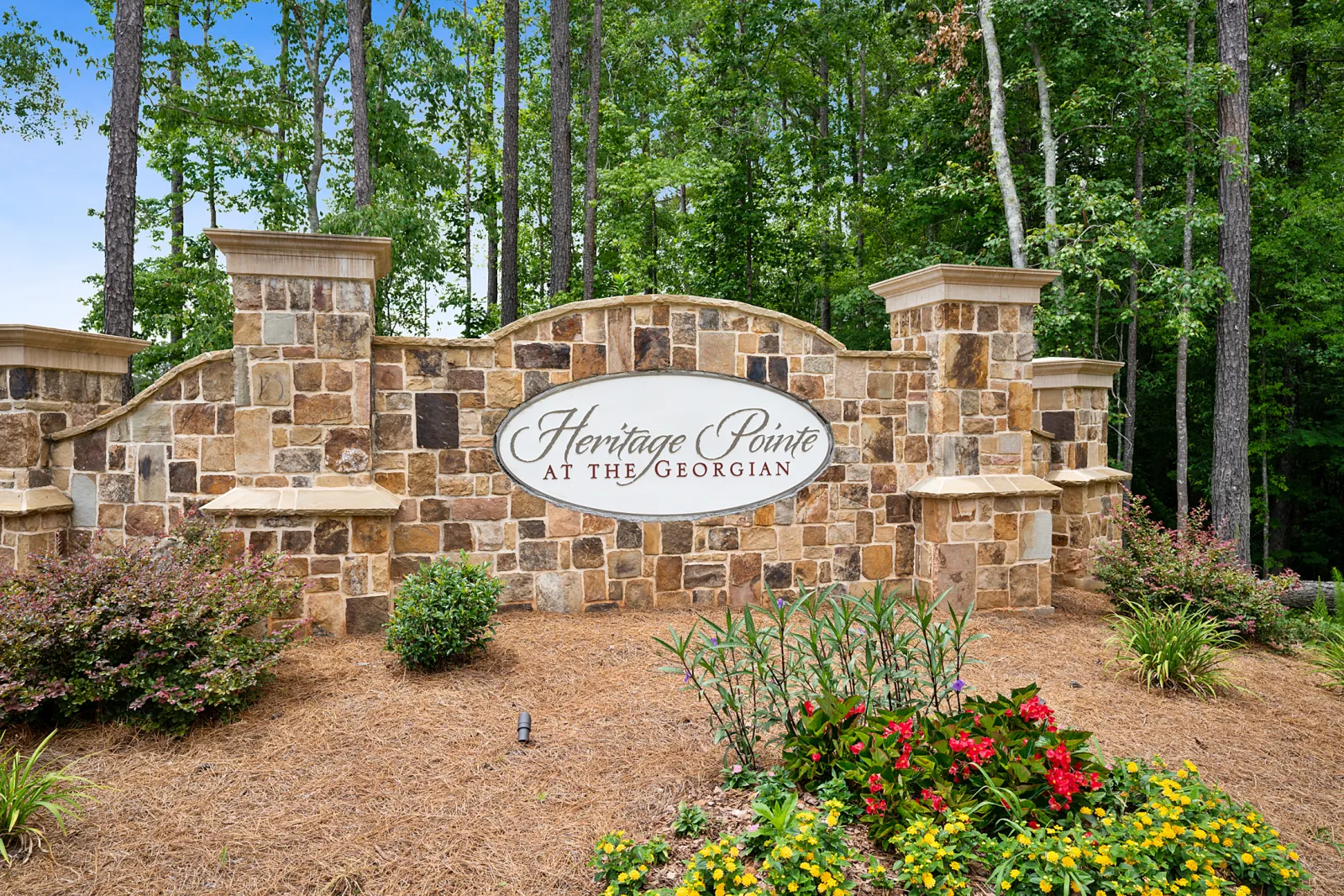 Stone entrance sign for Heritage Pointe at The Georgian surrounded by flowers and trees in a landscaped area.