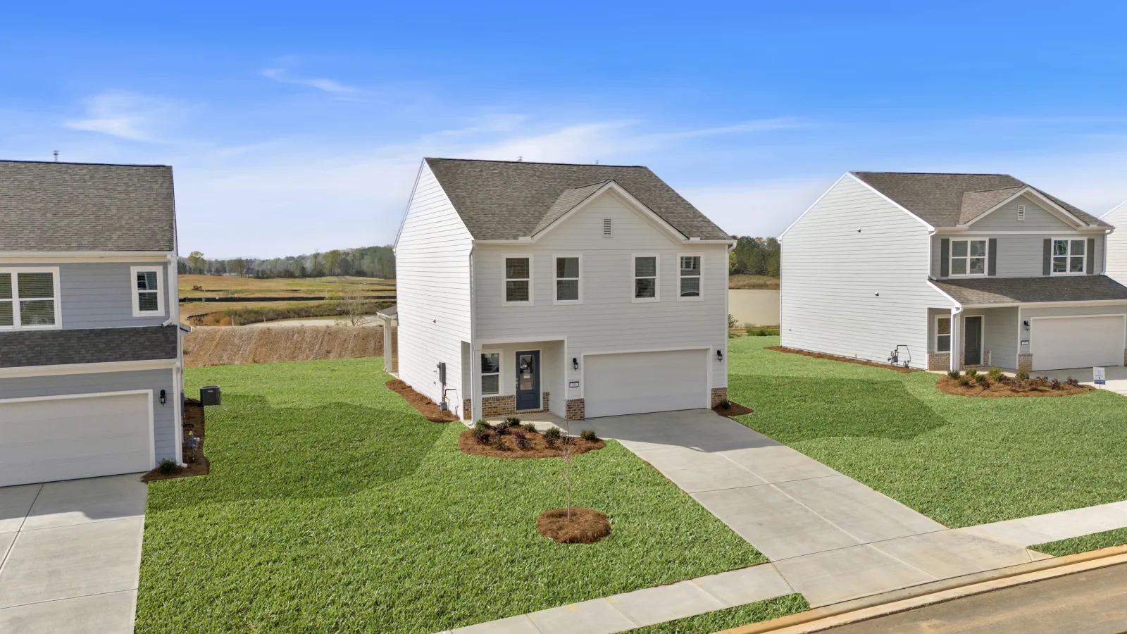 New suburban two-story white house with attached garage and neatly landscaped green lawn under blue sky.