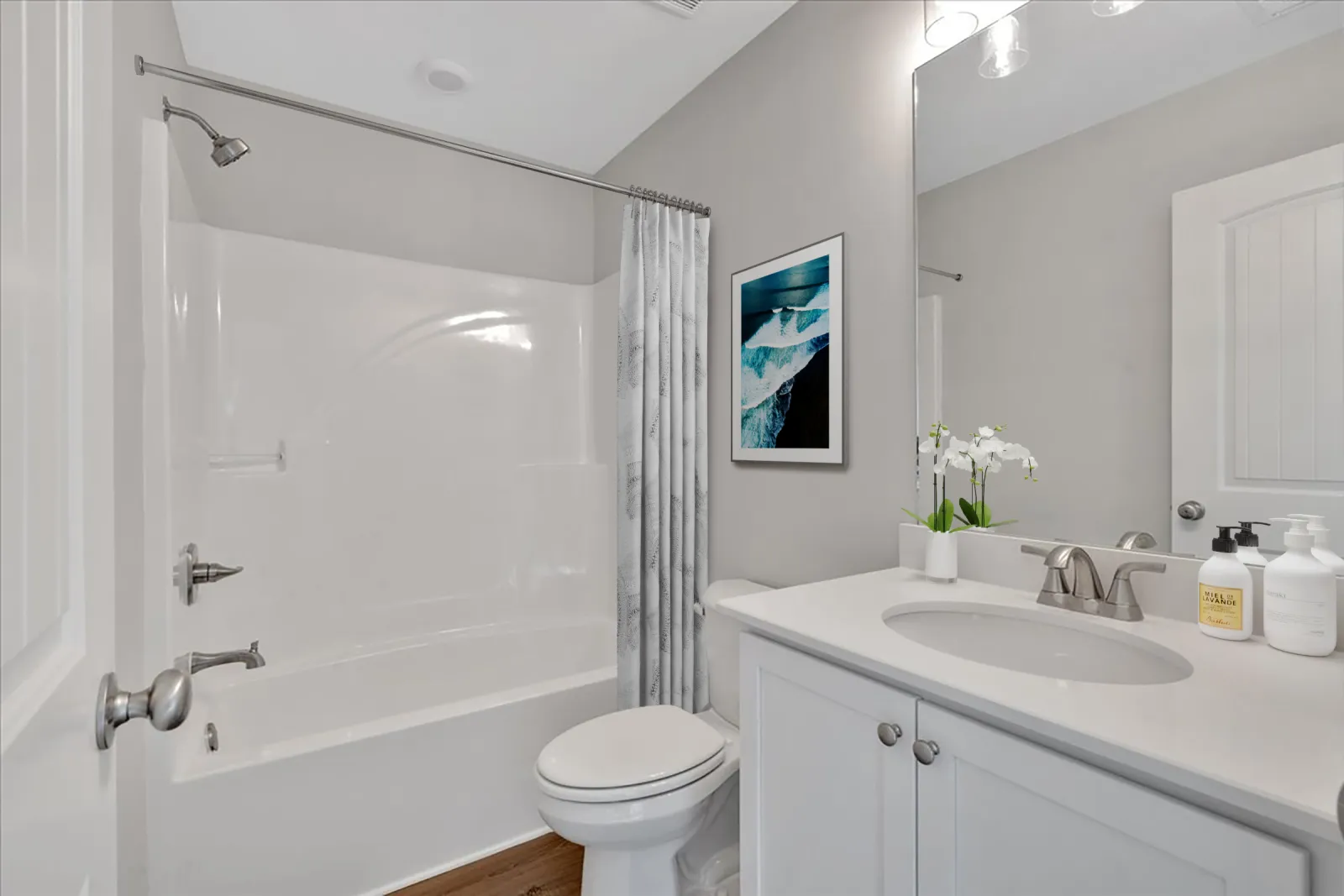 Modern clean bathroom with white bathtub, toilet, vanity with sink, mirror, and ocean wall art.