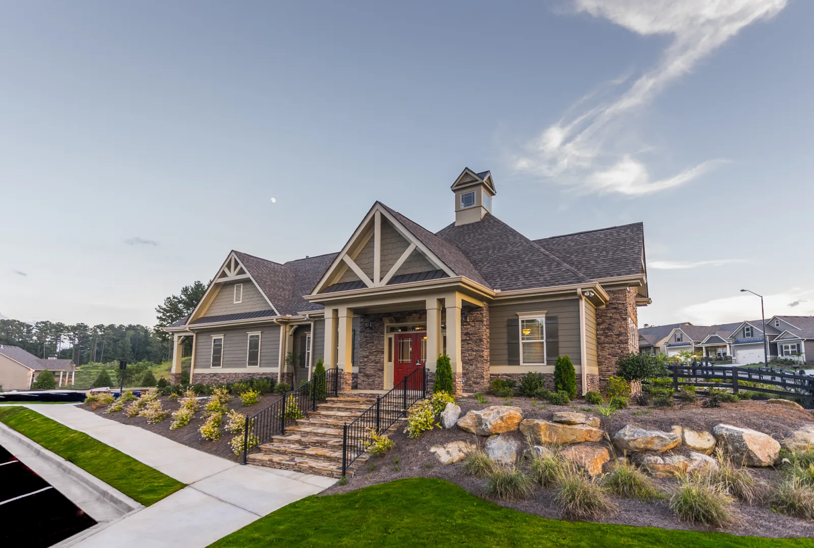 Modern suburban house with stone steps, landscaped garden, and a cloudy blue sky at dusk.