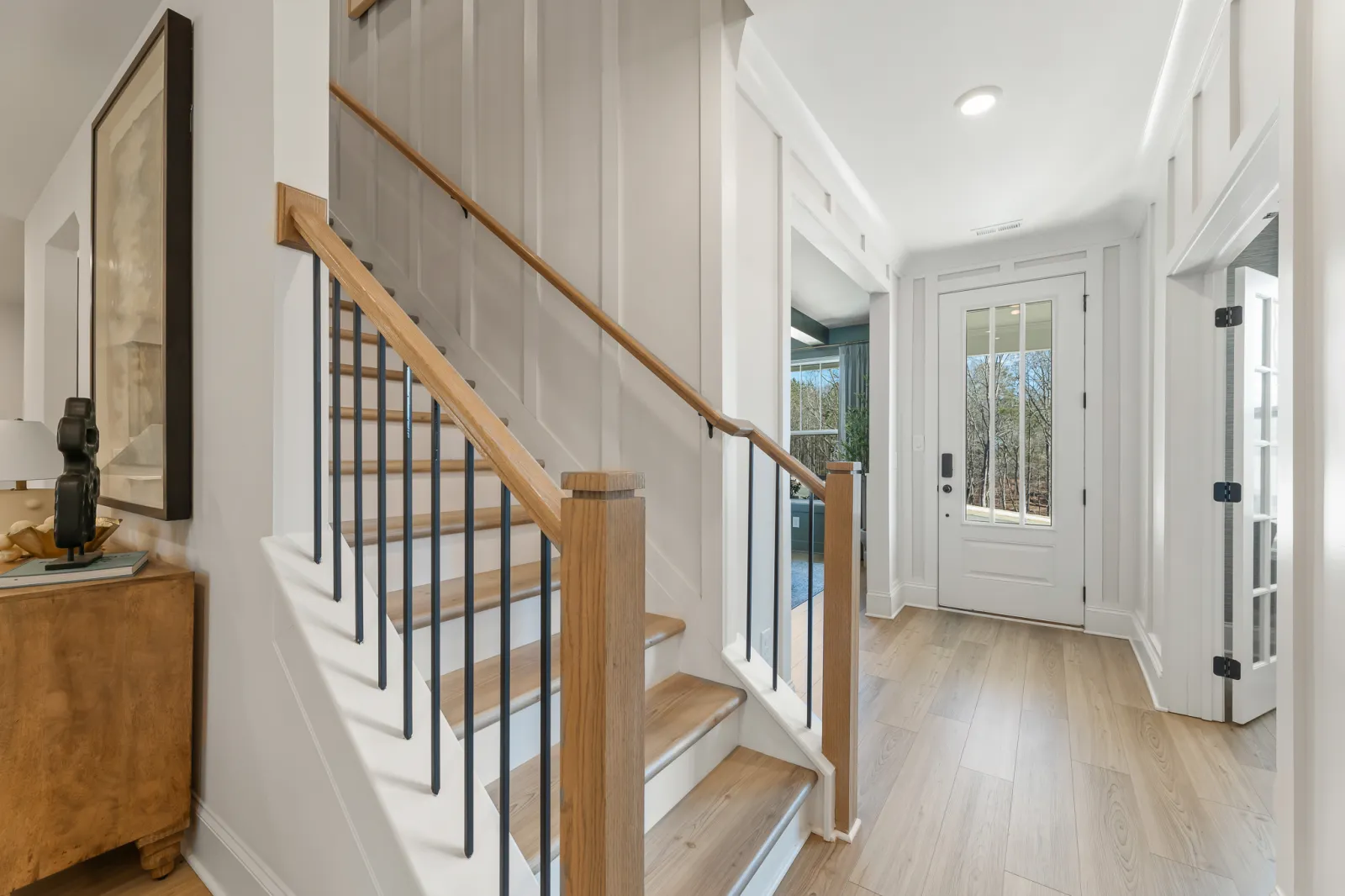 Bright modern entryway with wooden staircase, light hardwood floors, white walls, and a glass-paneled front door.