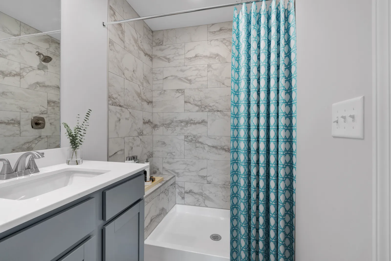Modern bathroom with marble tiled shower, white countertop vanity, blue cabinetry, and patterned blue shower curtain