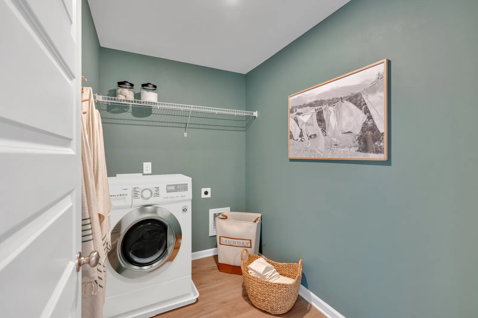 Bright laundry room featuring a washing machine, shelves, and decorative wall art.