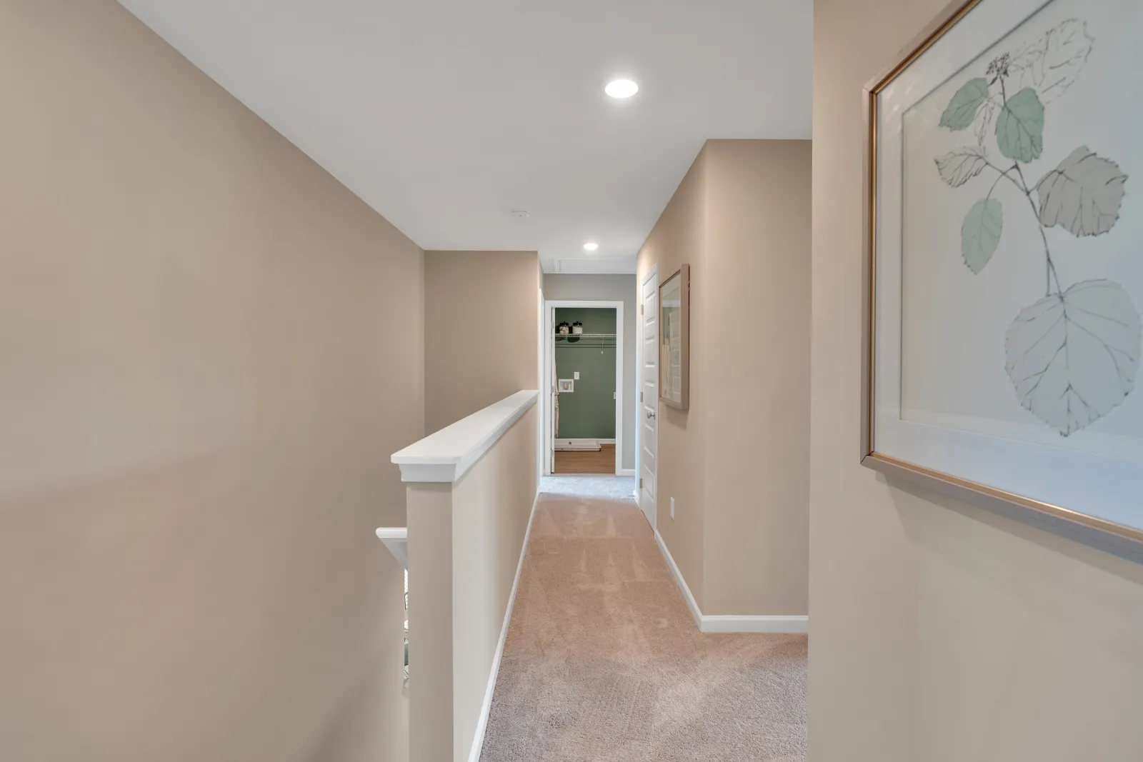 Bright hallway with neutral walls, carpet flooring, and framed artwork, leading to a green-themed room.