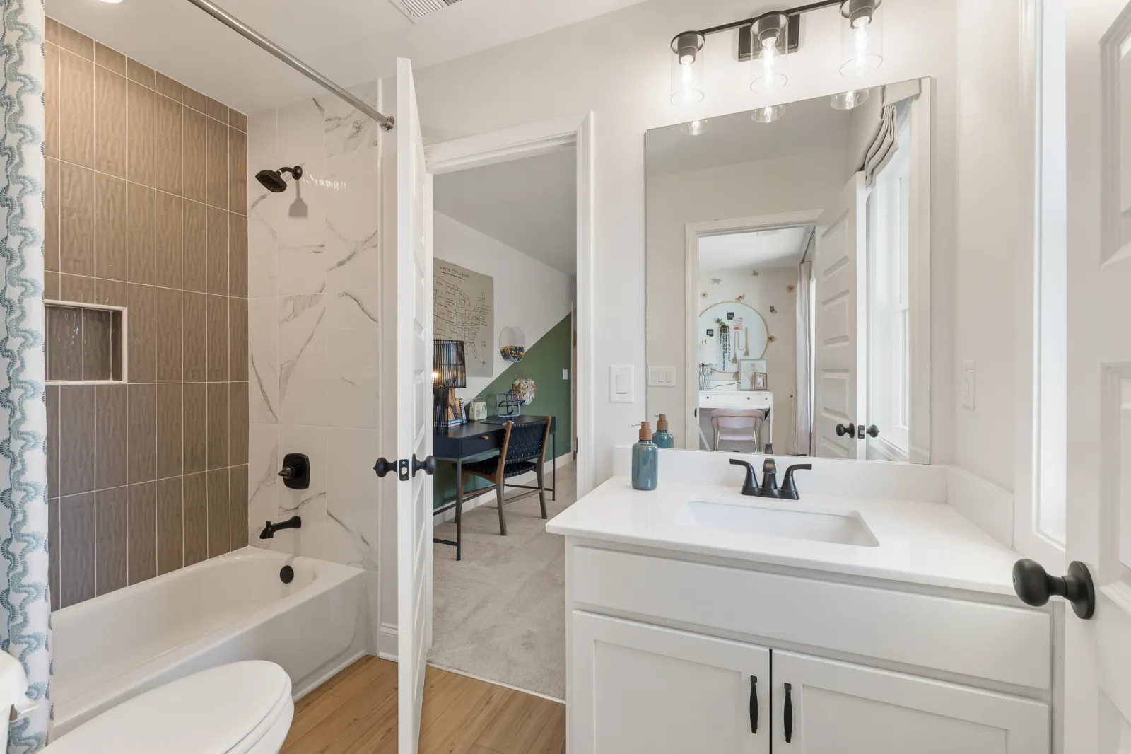 Bright bathroom with white vanity, black fixtures, bathtub with brown and white tile, and an open door to office space.