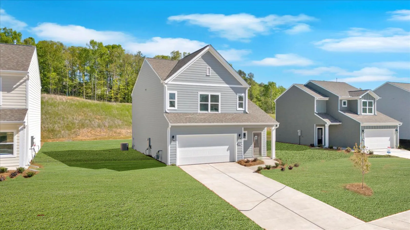 Newly built single-family homes with green lawns and clear blue skies in a suburban neighborhood.