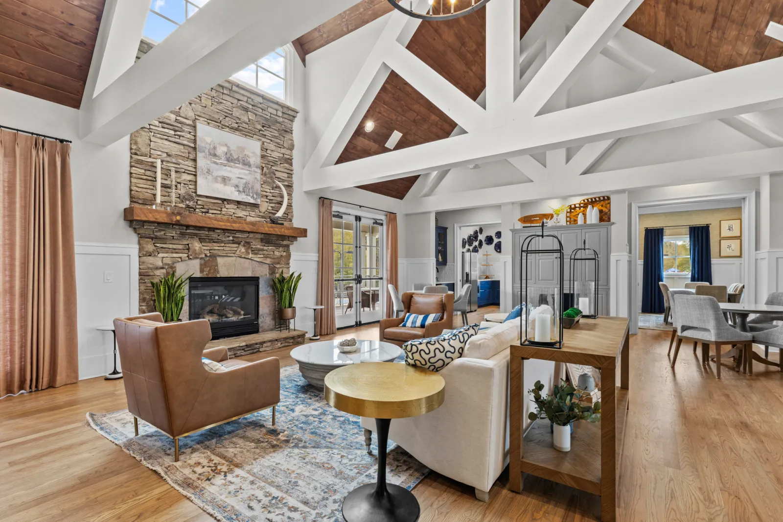 Spacious living room with vaulted wood ceilings, stone fireplace, leather chairs, and modern decor in natural light