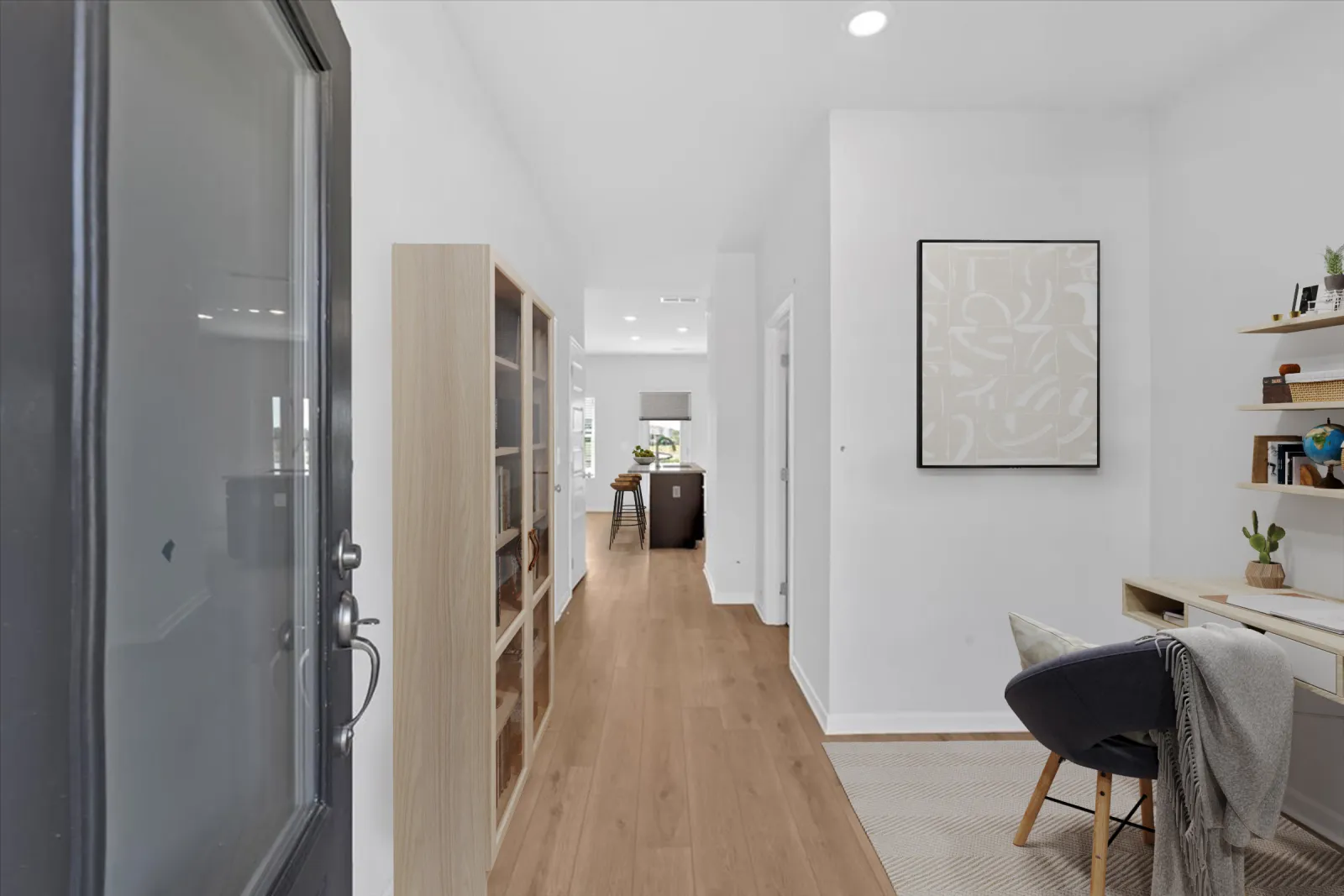 Bright modern hallway with wooden flooring, glass cabinet, desk area, and open kitchen in the background