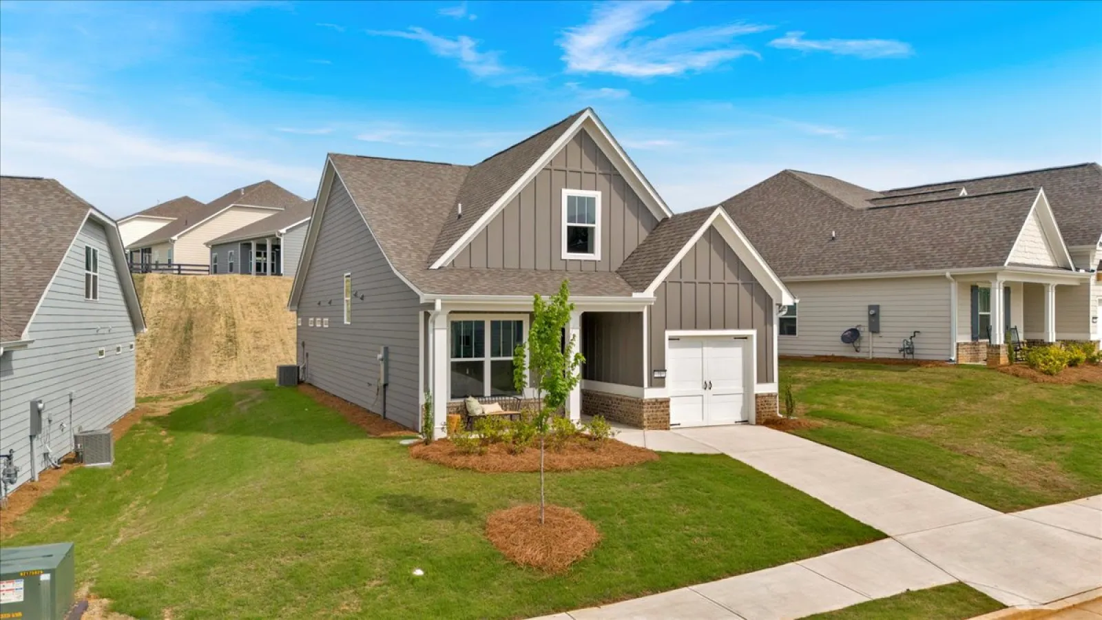 Modern single-family home with gray siding, garage, and manicured lawn on a sunny day with blue sky.