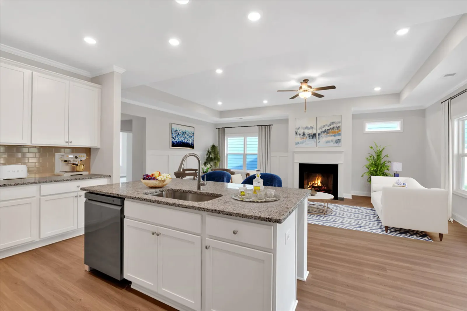 Modern open kitchen and living room with white cabinets, granite island, hardwood floors, and cozy fireplace.