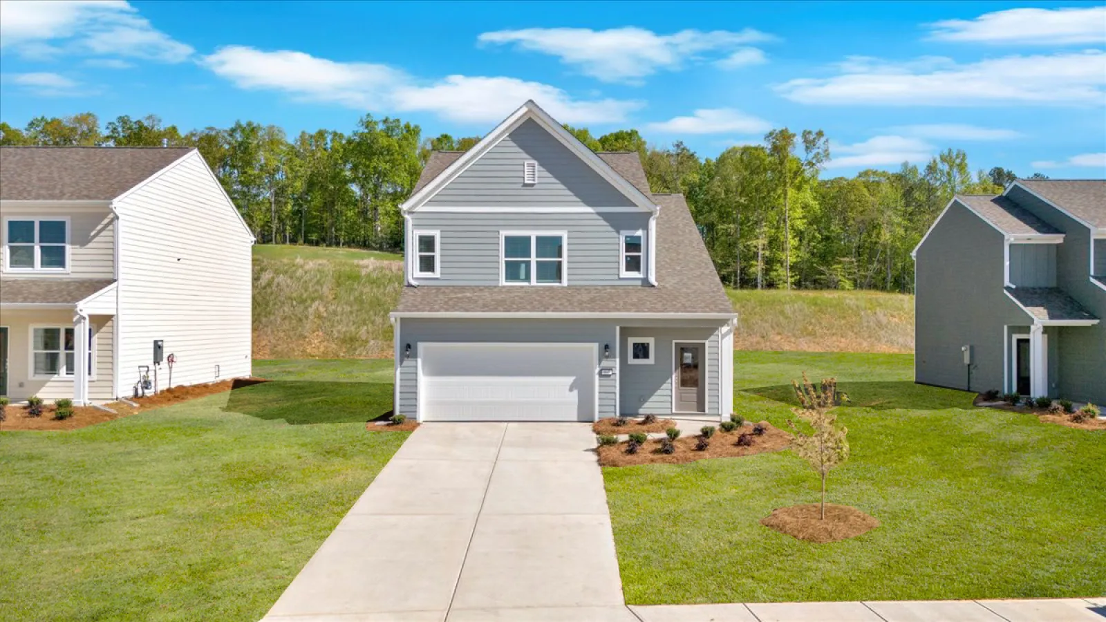 Modern two-story gray house with white trim, garage, and a manicured lawn under a blue sky.