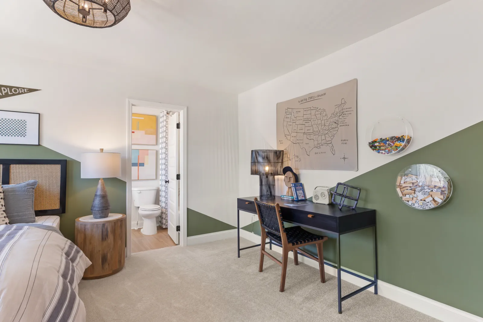 Modern bedroom with green and white walls, a study desk, chair, bedside lamp, and open bathroom door.