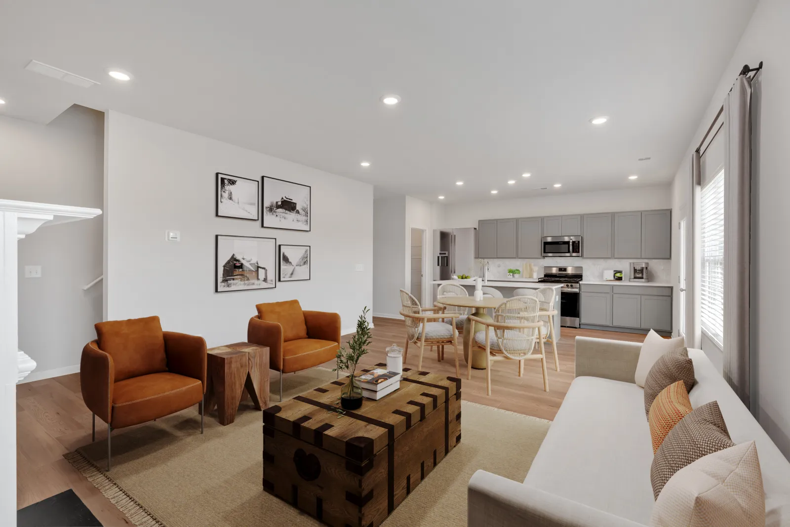 Modern open living room with brown armchairs, white sofa, wooden coffee table, dining area, and gray kitchen cabinets.