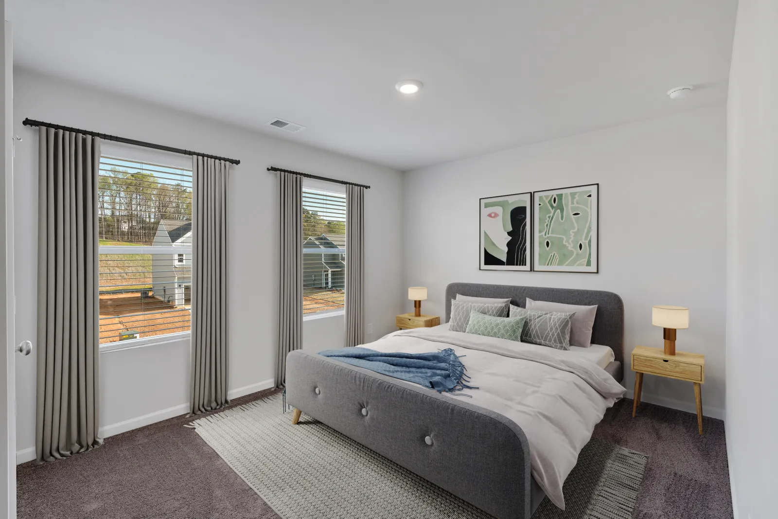 Modern bedroom with gray upholstered bed, abstract wall art, two windows with curtains, and wooden nightstands with lamps.