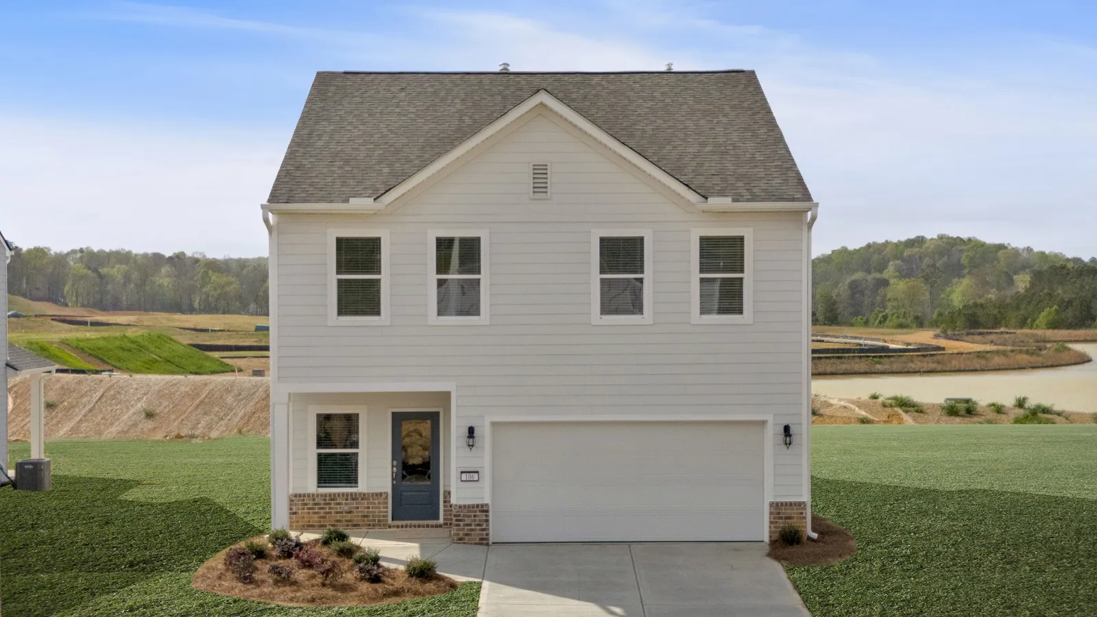 Two-story white house with double garage and blue front door on a newly developed grassy lot.