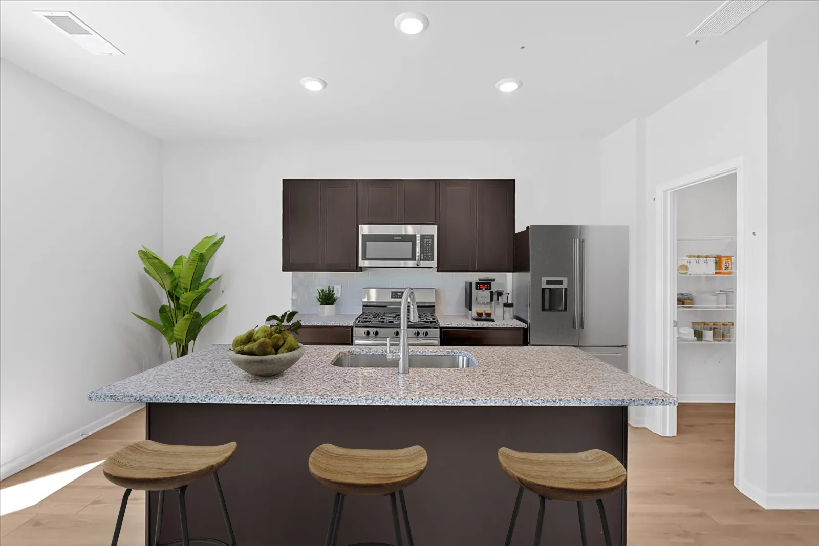 Modern kitchen with dark cabinets, stainless steel appliances, granite island, three stools, and pantry door open.